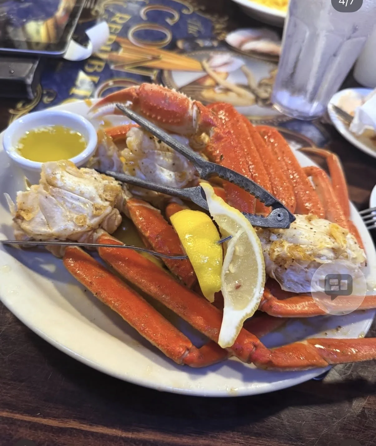 Plate of cooked crab with lemon wedge, lemon slices, melted butter, and metal crab tongs on a restaurant table.