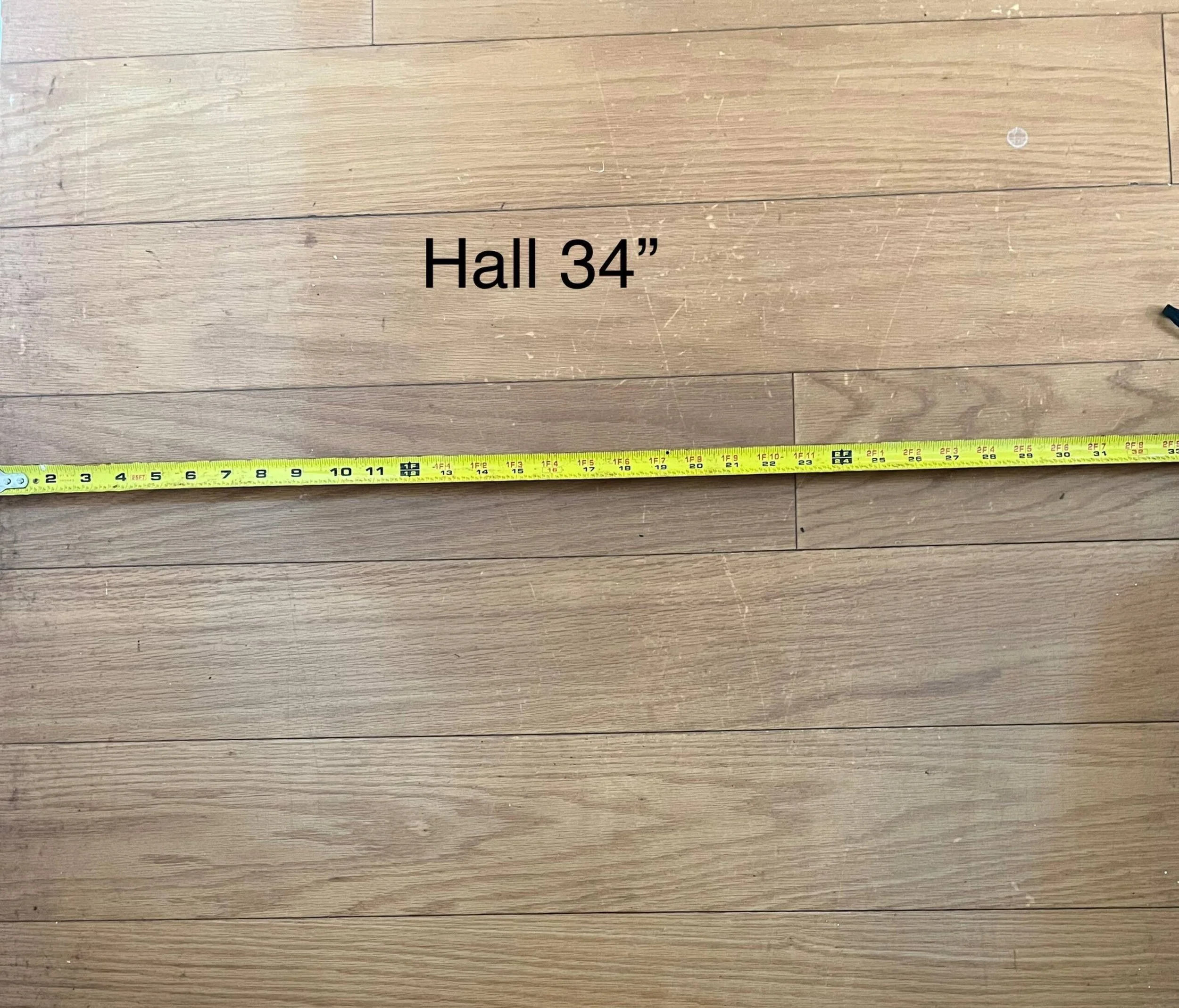Wooden floor with a yellow tape measure extended across it. Text on the image says 'Hall 34"'.