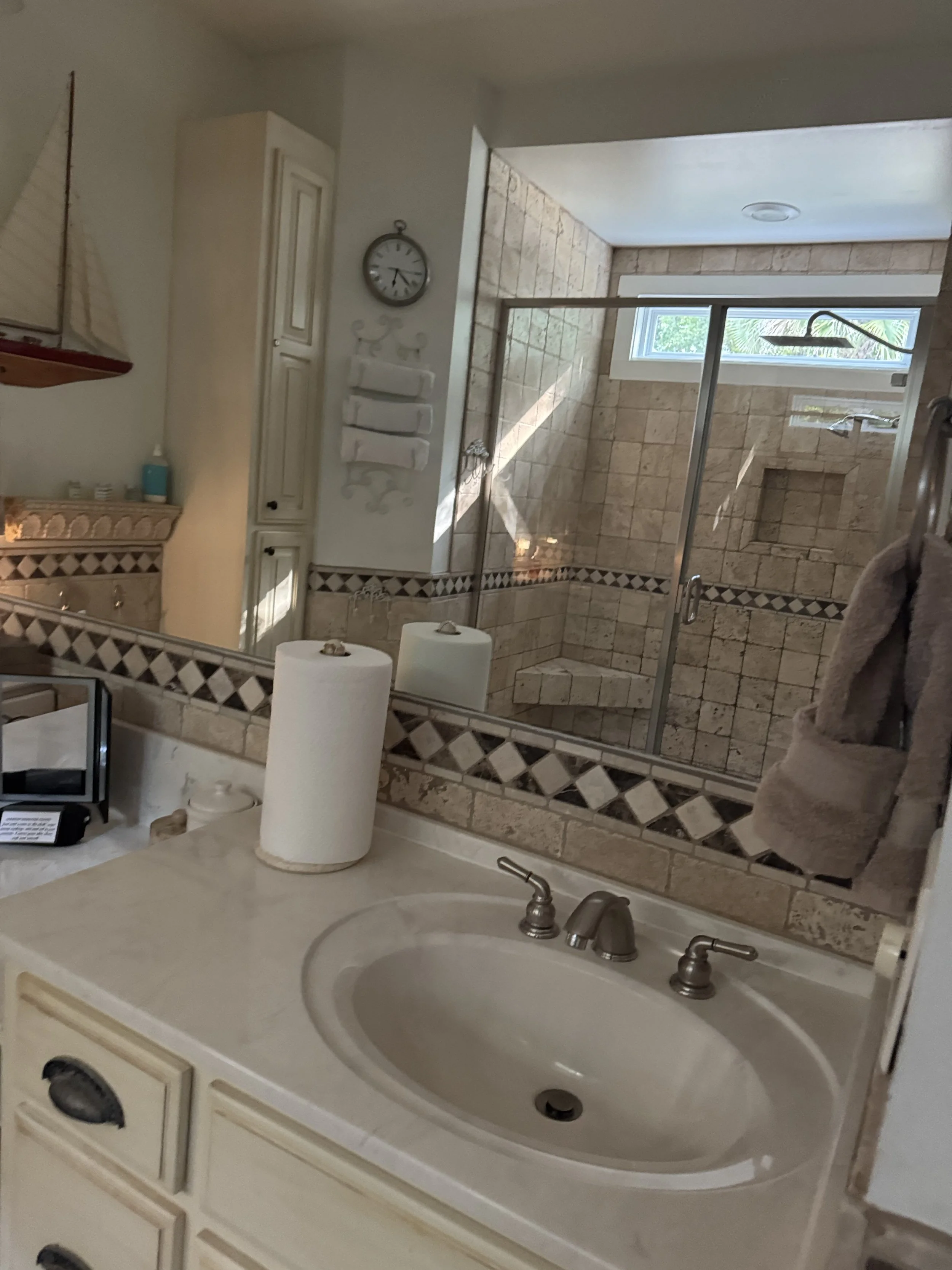 Bathroom with a white sink vanity, a mirror, beige tiled shower with glass door, and a small window with natural light.