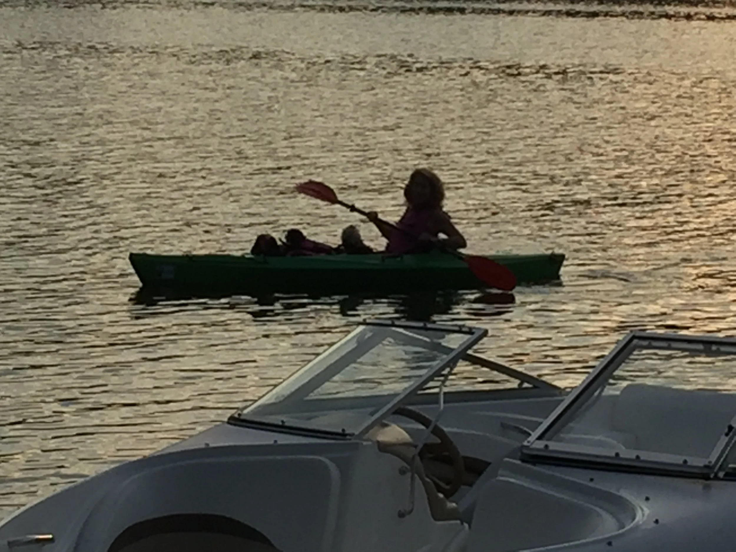 Person kayaking on a calm body of water during sunset, with lounge chairs in the foreground.