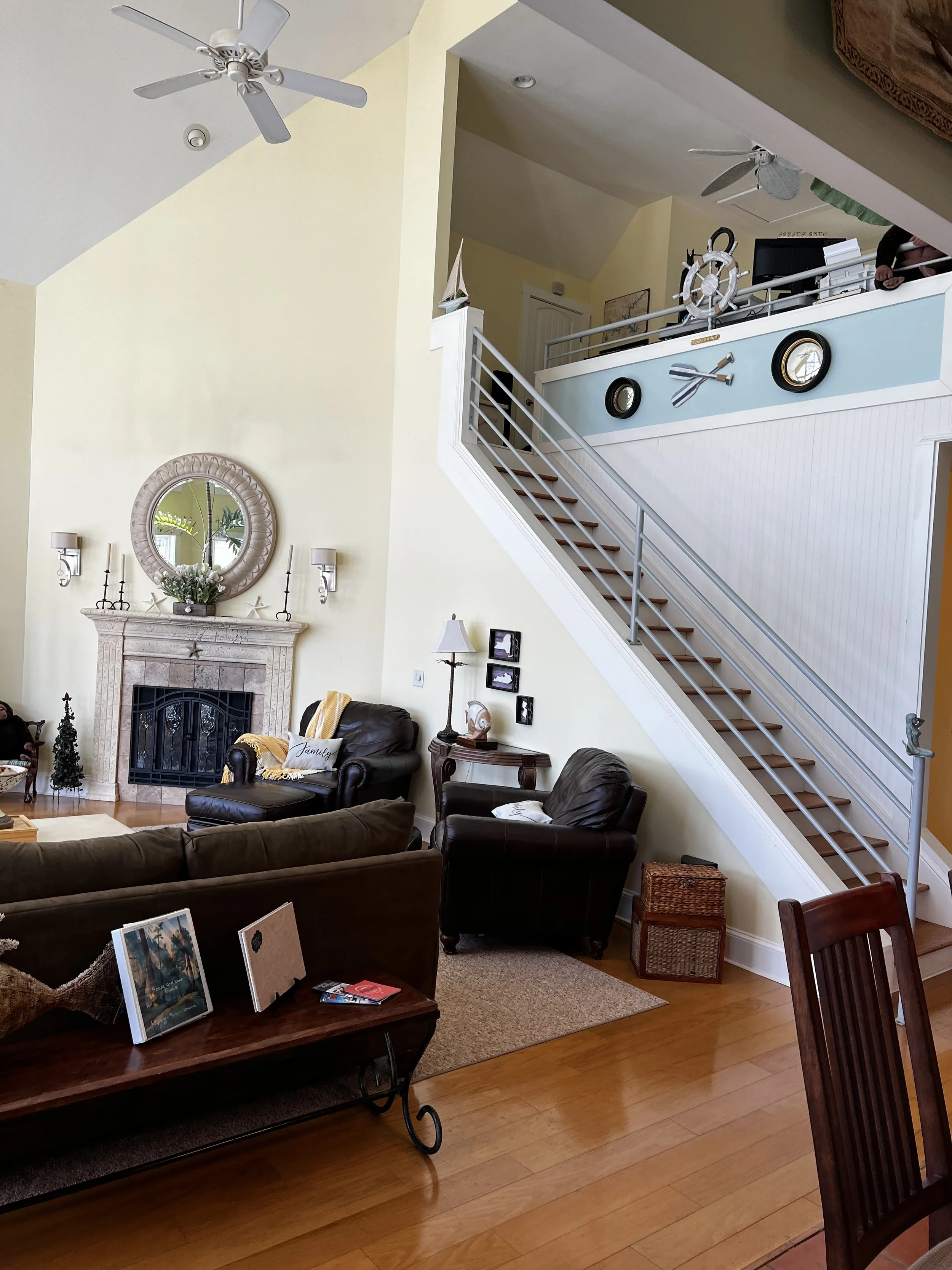 Living room with a fireplace, multiple chairs, a staircase, and nautical decorations on the wall.