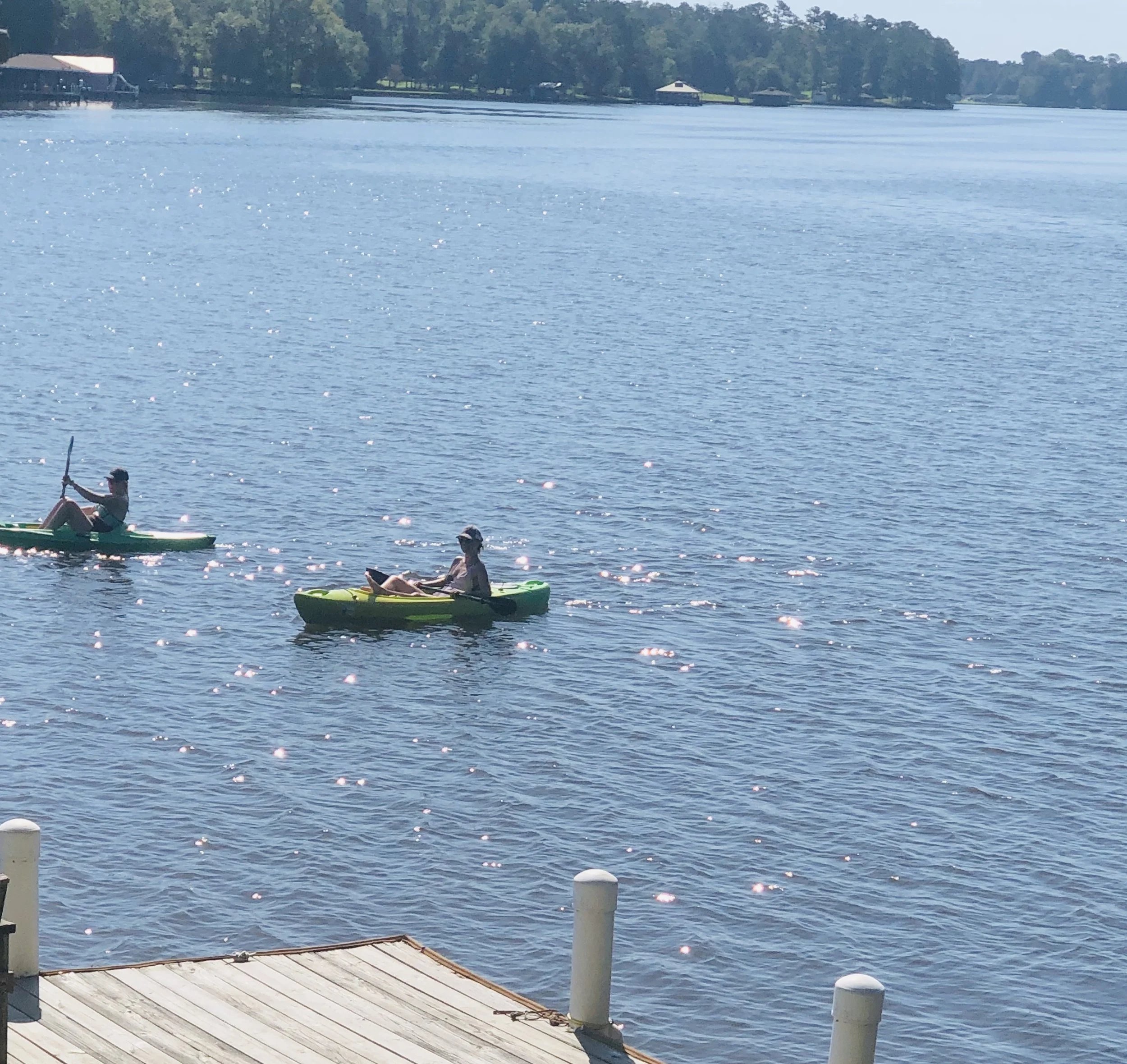 People kayaking on a lake with trees and small docks in the background, bright sunny day.