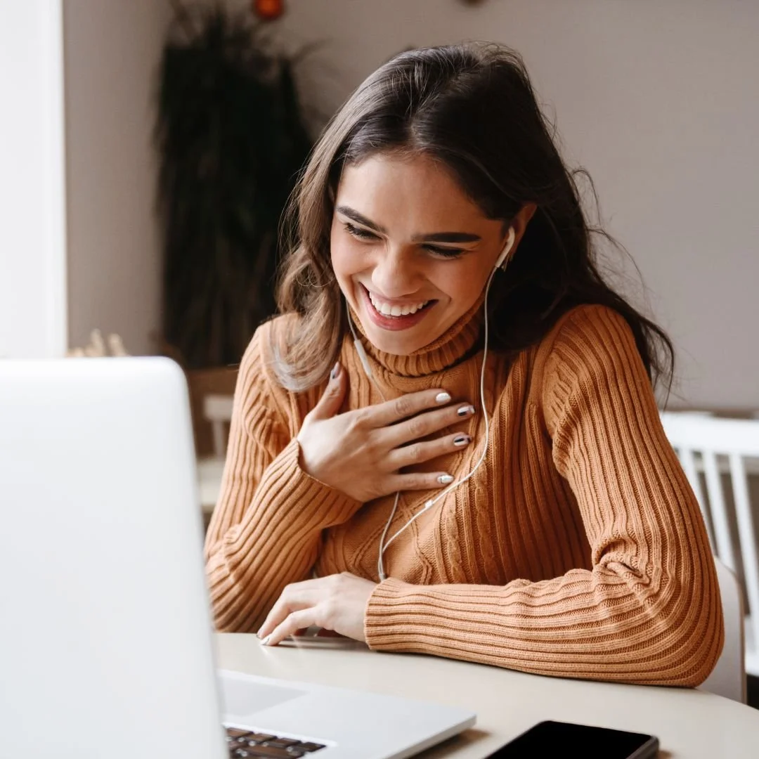 woman with black hair smiling at laptop, with hand on chest