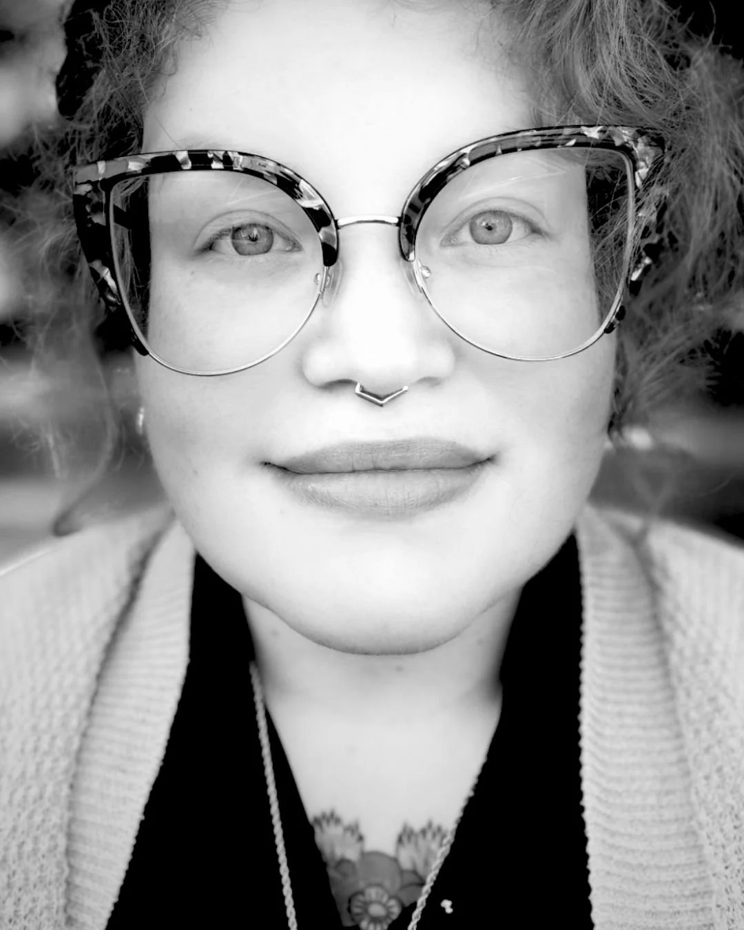 black and white photo of a white woman with large glasses and septum ring smiling