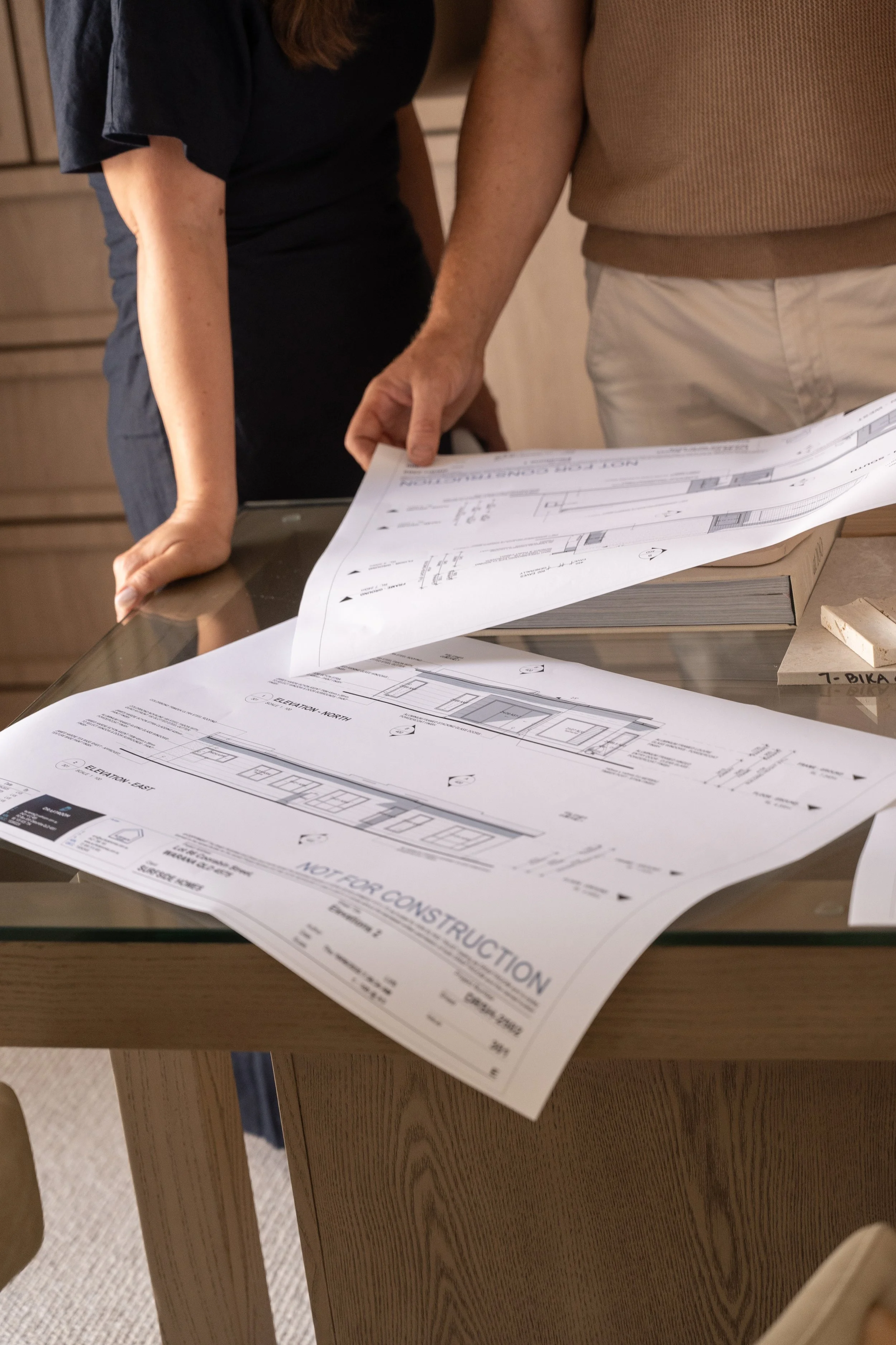 Two people looking at architectural blueprints on a wooden table.
