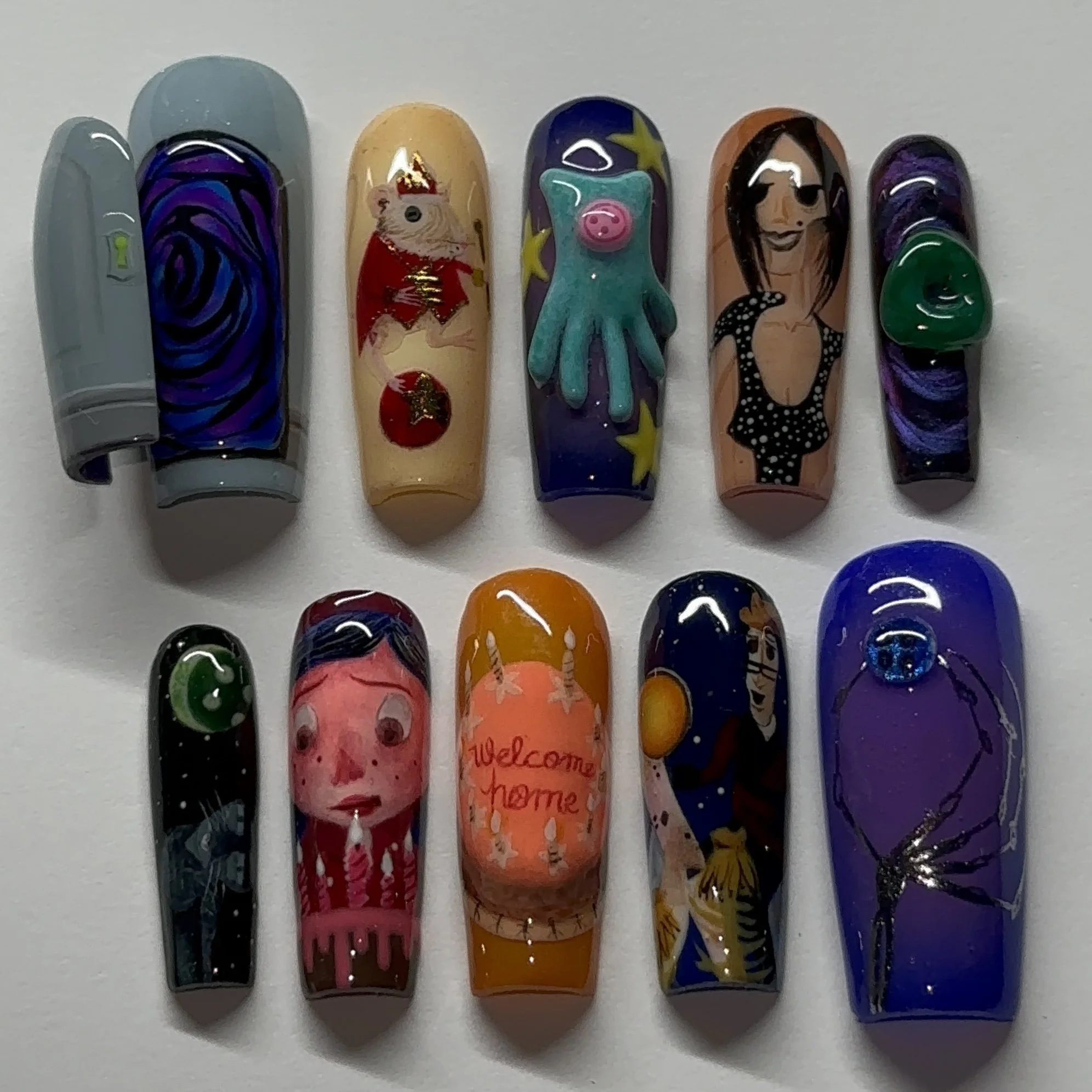 Collection of painting decorated nail tips with festive, artistic, and character designs, including a pig, a woman, a unicorn, an abstract pattern, and other colorful motifs.