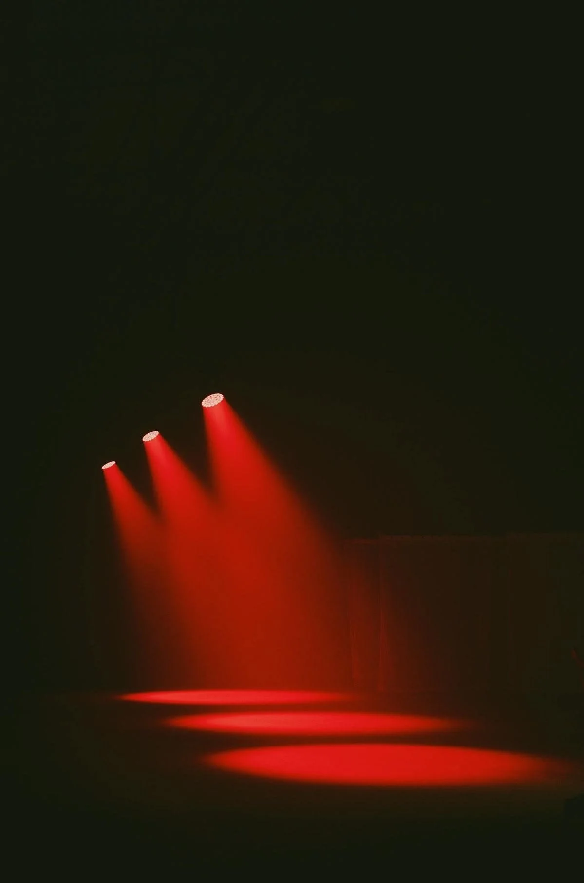 Three red spotlights shining downward onto a stage with a red reflection.