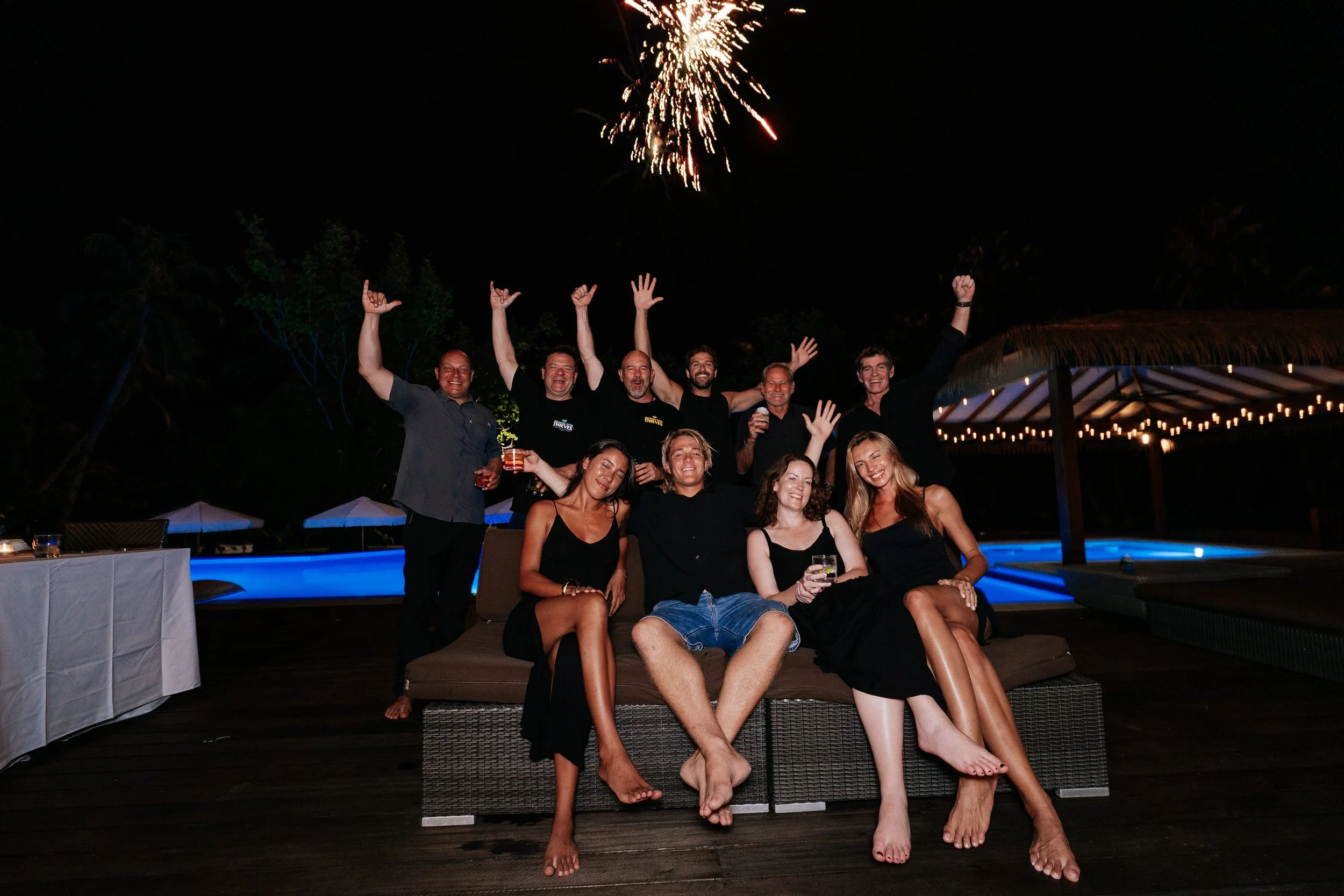Guests celebrate at a nighttime pool party at Tanah Mympi, posing together as a sparkler lights up the sky.
