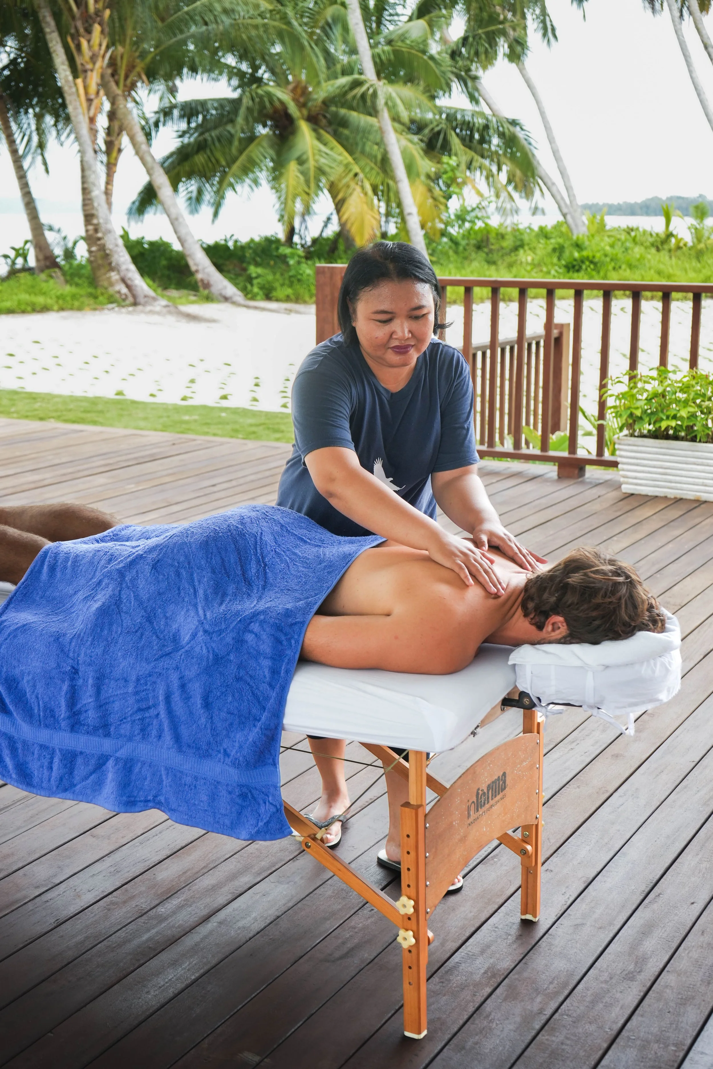 A guest receives an outdoor massage on a wooden deck at Tanah Mympi, wrapped in a blue towel.