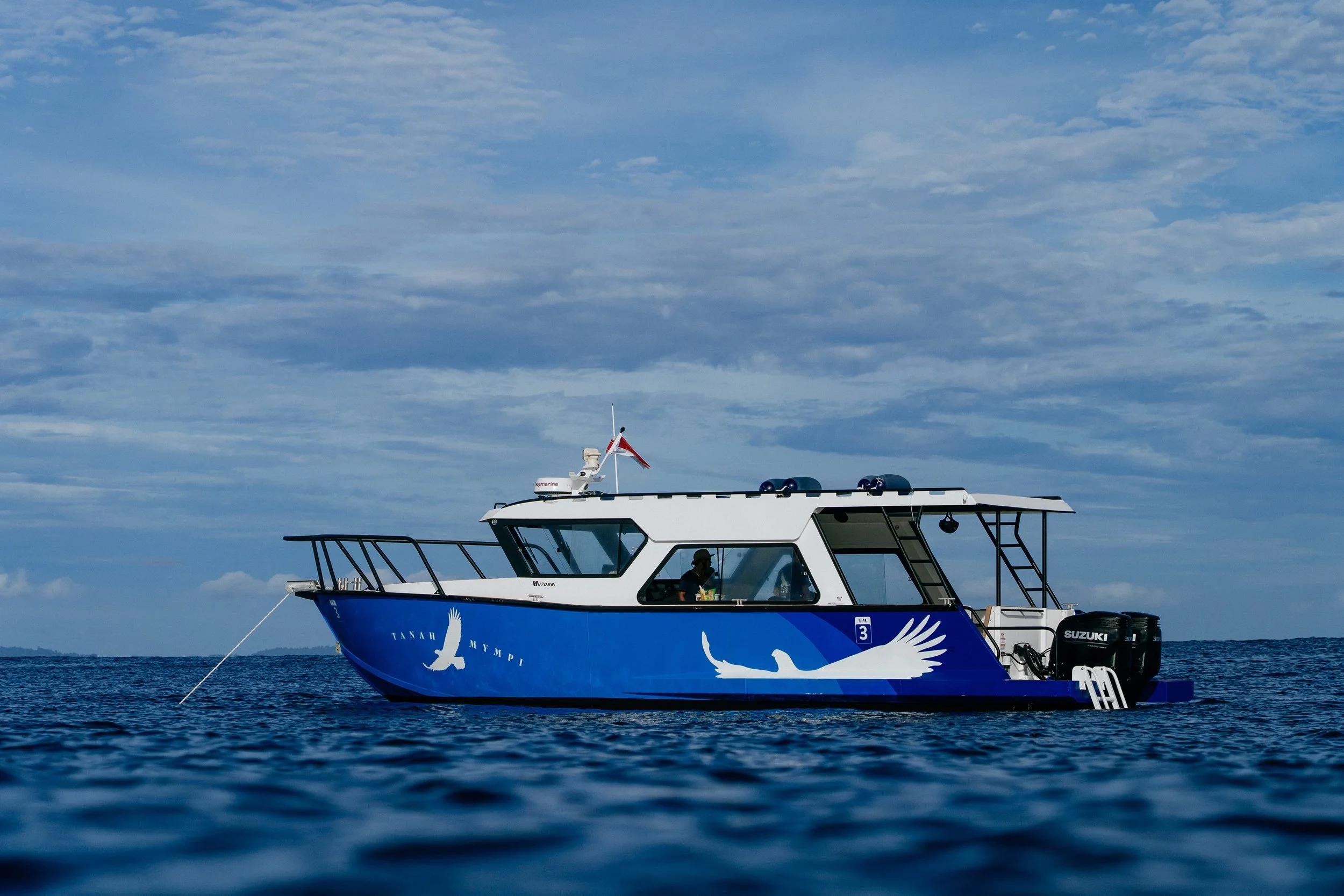 A Tanah Mympi boat out on open water, seen against the horizon.