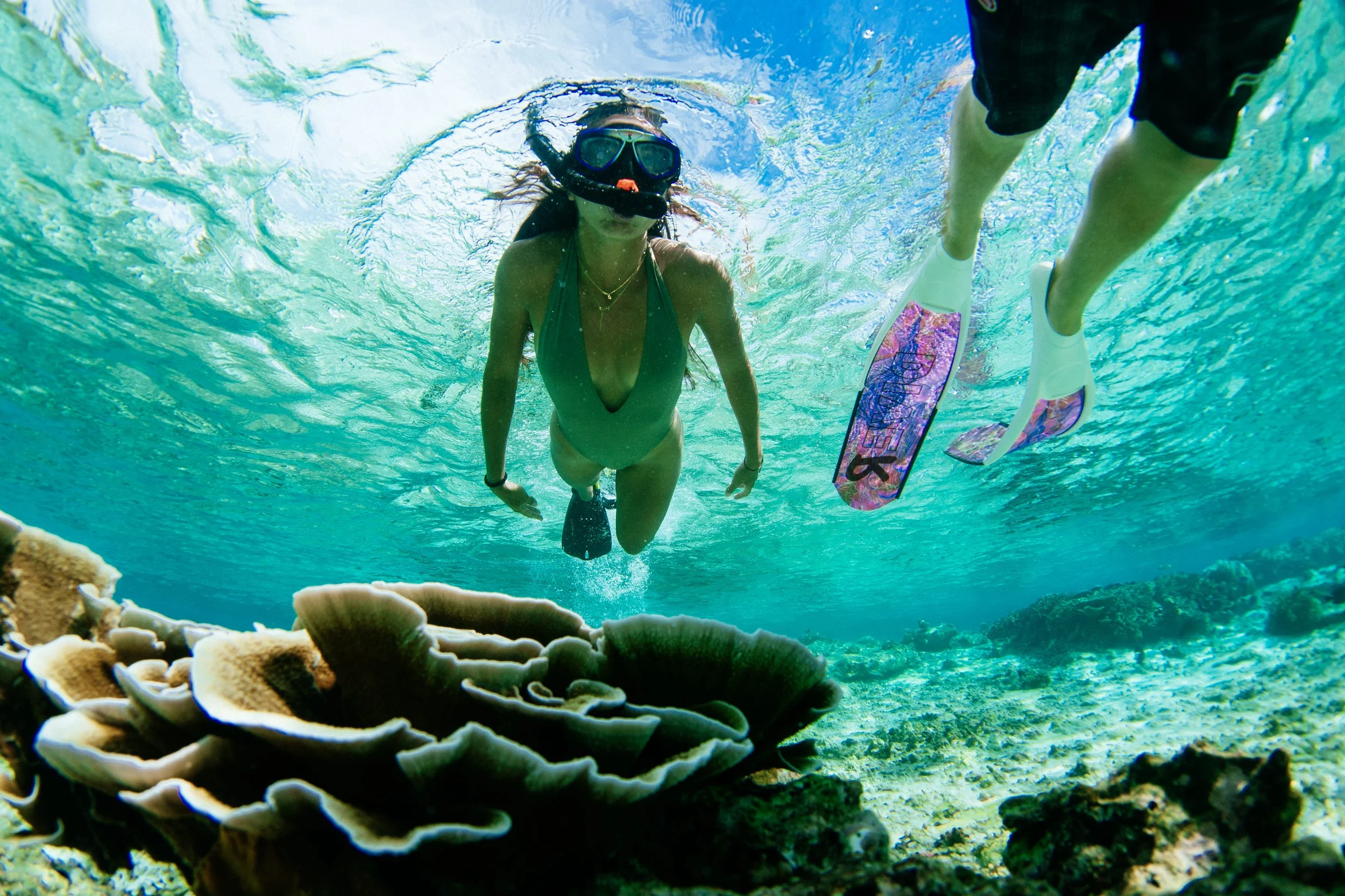 A snorkeler explores a colorful coral reef near Tanah Mympi, with reef and sand bottoms visible underwater.