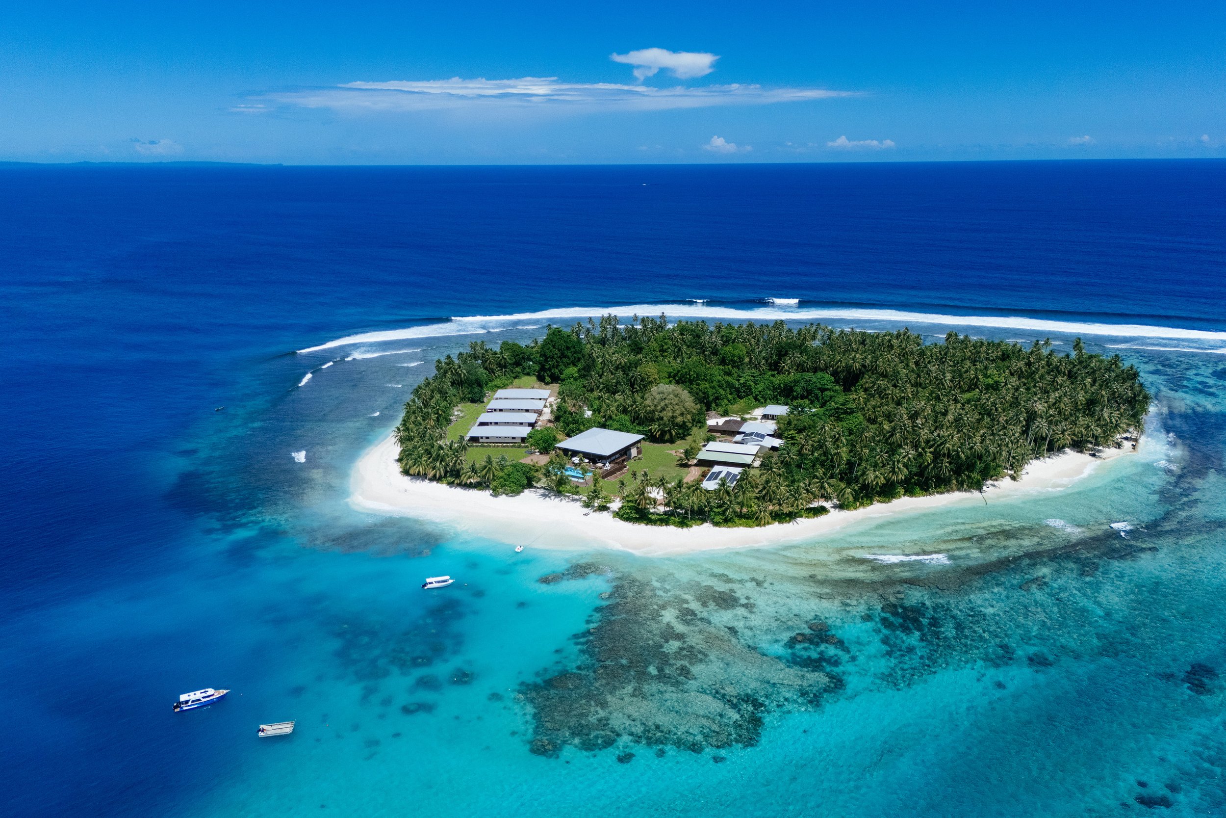 An aerial view of Tanah Mympi's private island, its palm covered shoreline ringed by shallow turquoise reef in the Telo Islands.
