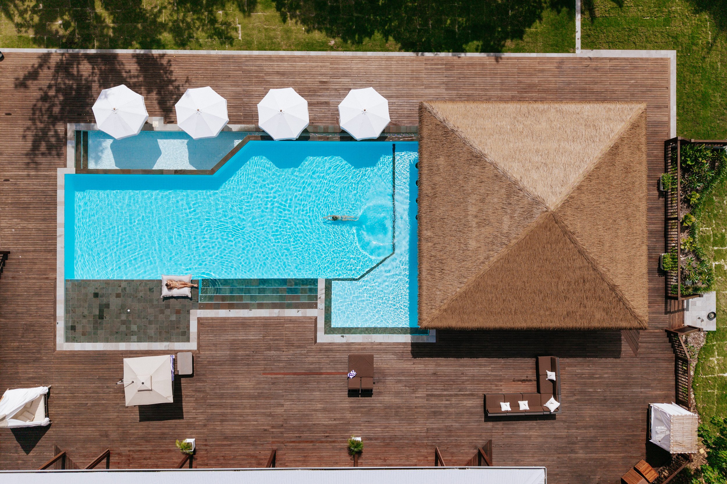 An aerial view of the pool and thatched pavilion at Tanah Mympi, with sun loungers and umbrellas along the deck.
