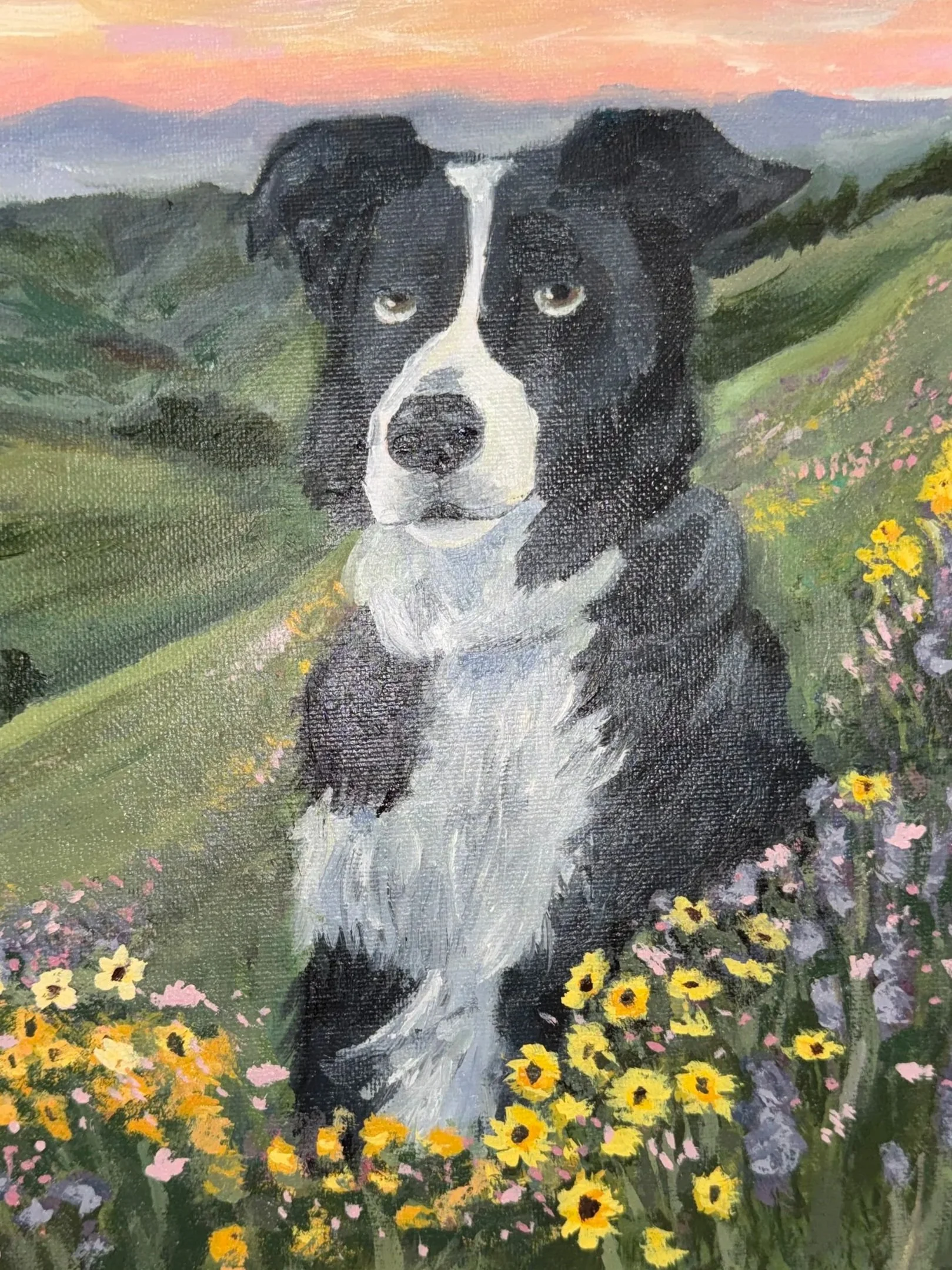 Painting of a black and white dog, likely a Border Collie, sitting amid colorful yellow, pink, and purple flowers on a green field with mountains and a pink sky in the background.