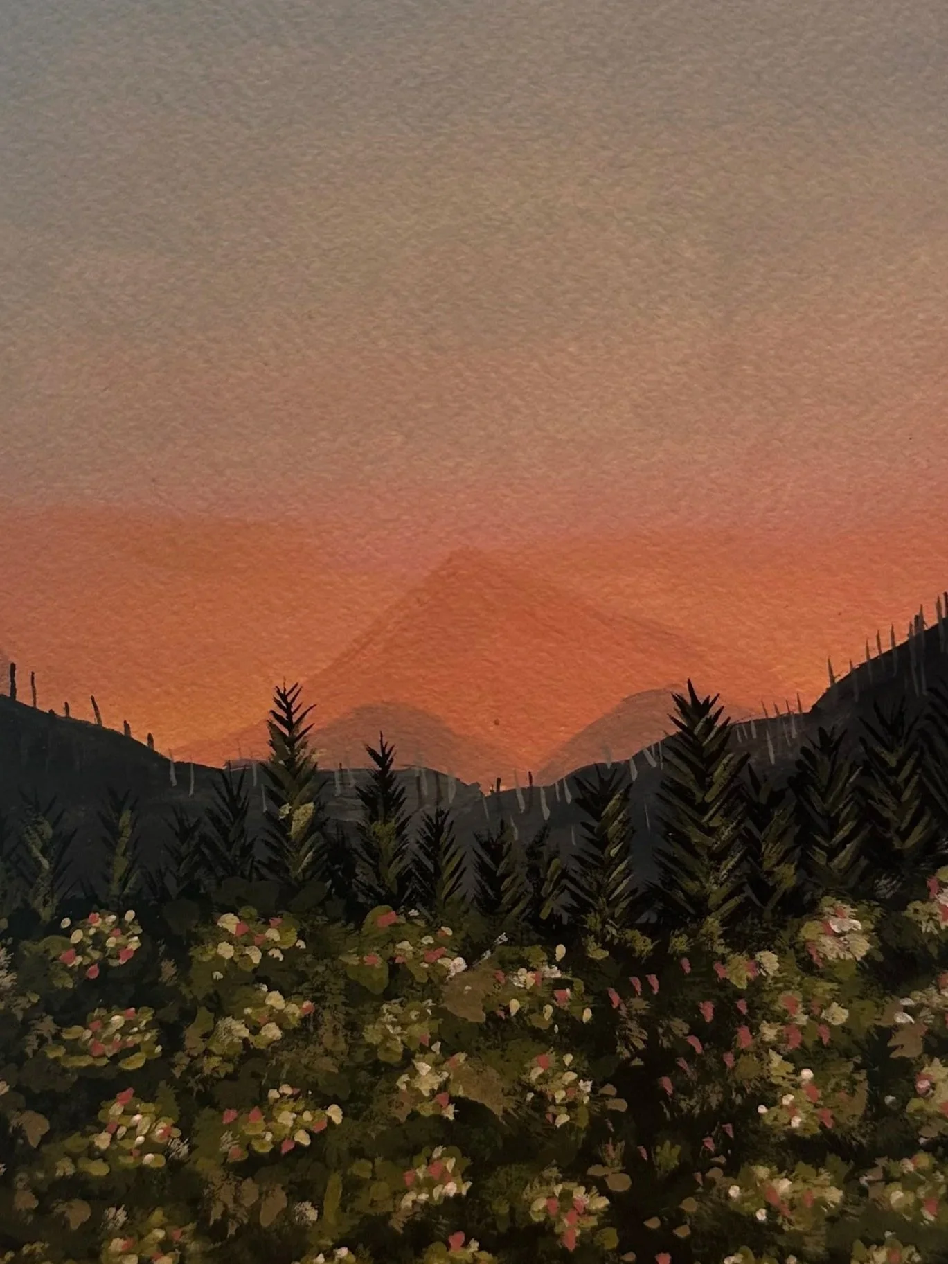 Sunset sky with orange and gray hues over a silhouette of trees and mountains, with a foreground of flowering plants.