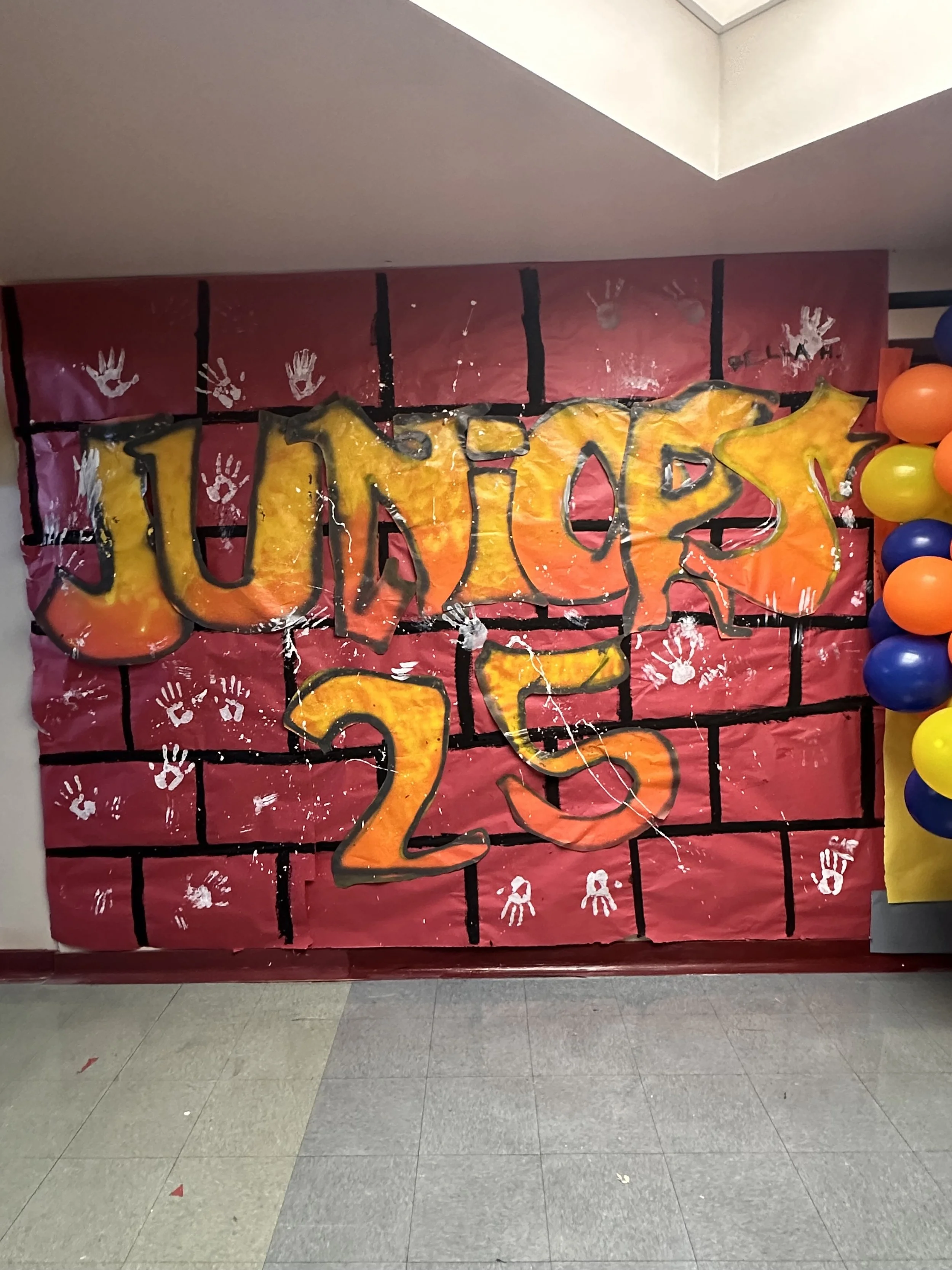 Decorative school-themed wall with graffiti, large orange and yellow letters spelling "Jump" and heaping balloon column on the right.
