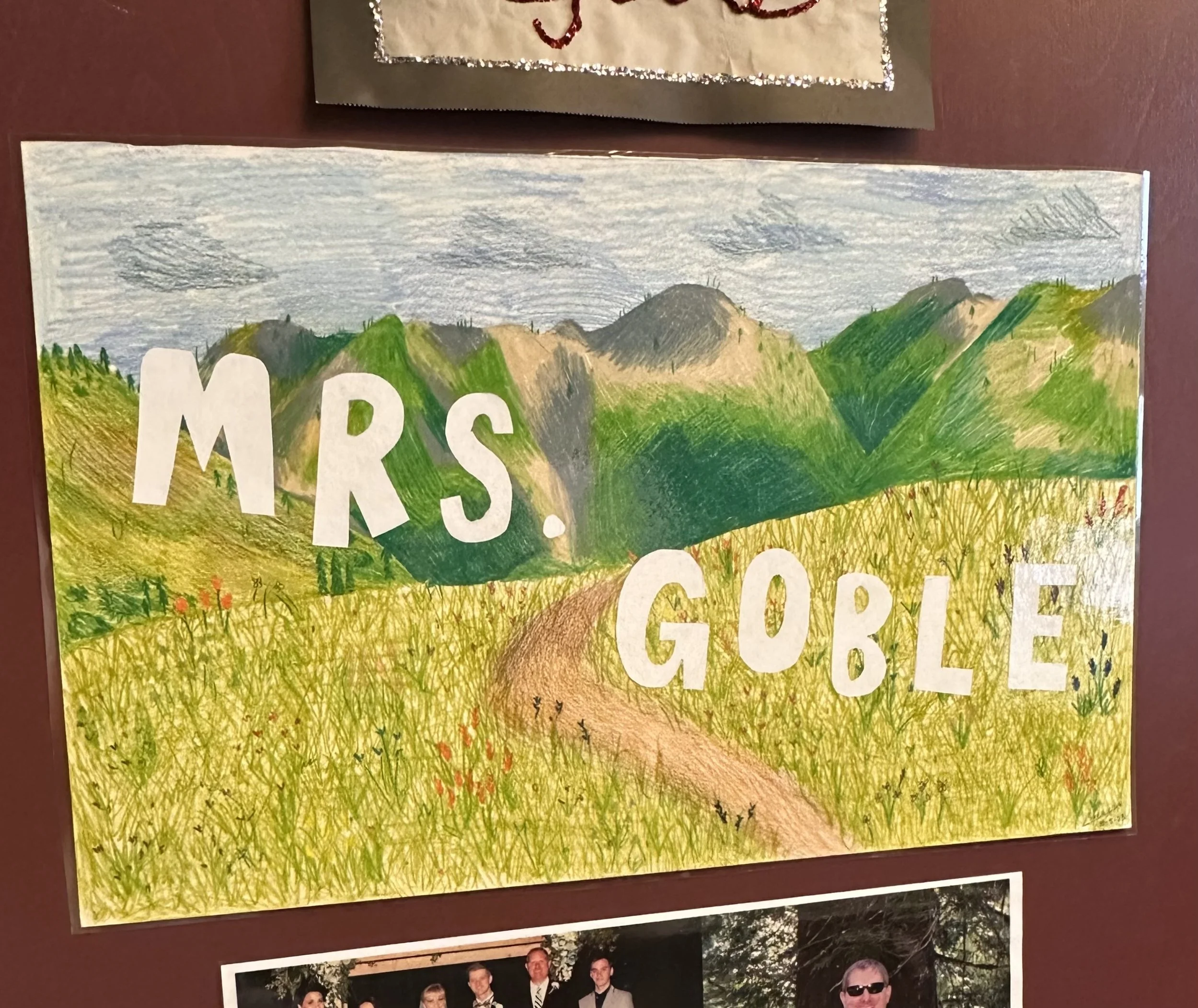 Colorful hand-drawn outdoor scene with mountains, trees, and grass, featuring part of a word "MRS" in large white letters.