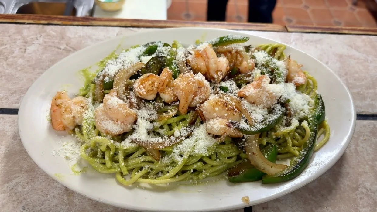 Plate of shrimp and vegetable lo mein noodles topped with grated cheese on a restaurant table
