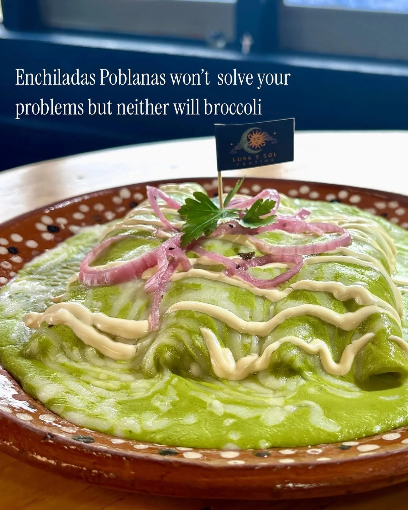 A plate of guacamole garnished with sliced red onions, a sprig of cilantro, and drizzled with mayonnaise, served on a decorative ceramic plate.