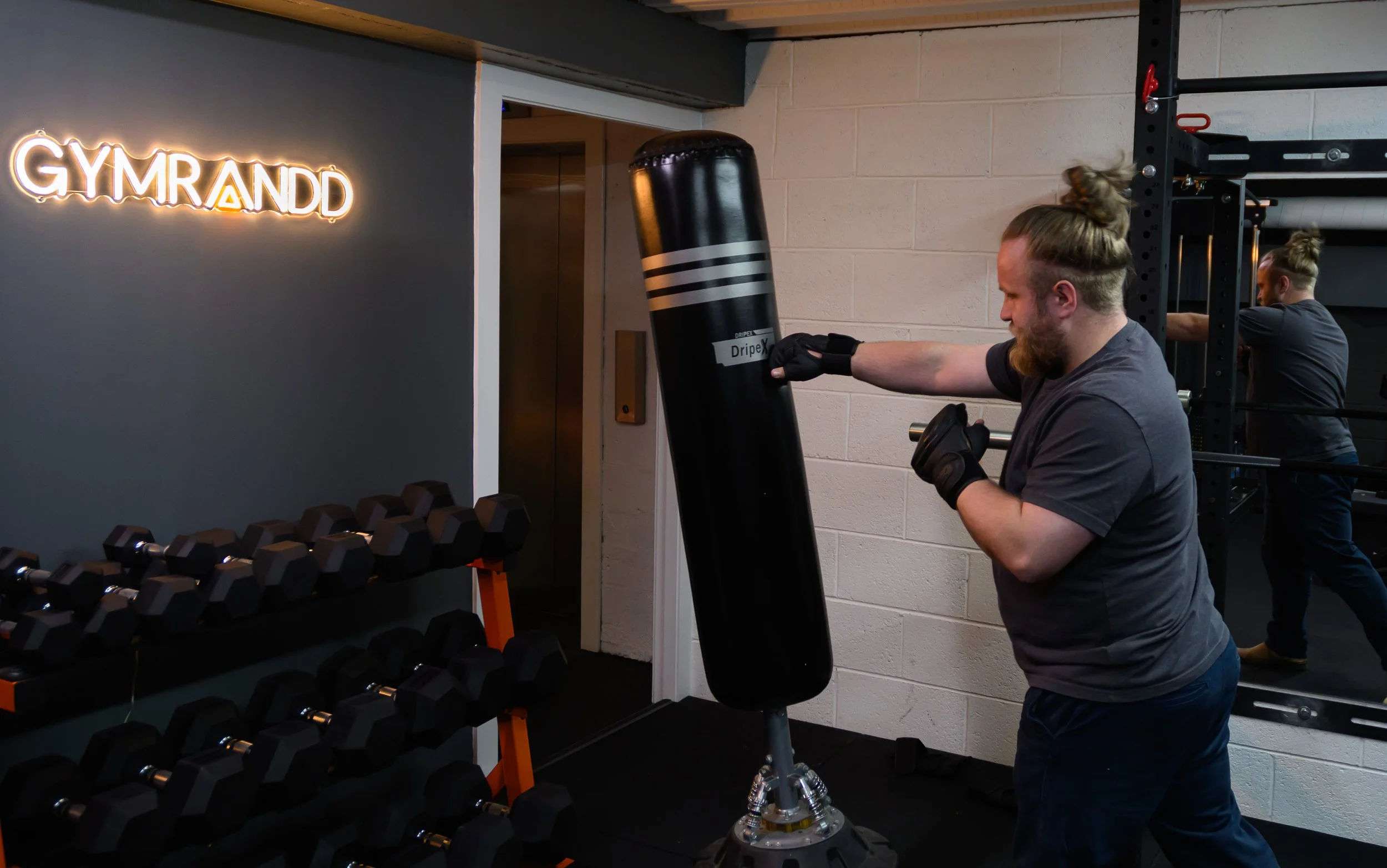 IMRANDD team member hitting a punch bag in the company gym, with weights and the GYMRANDD sign visible.