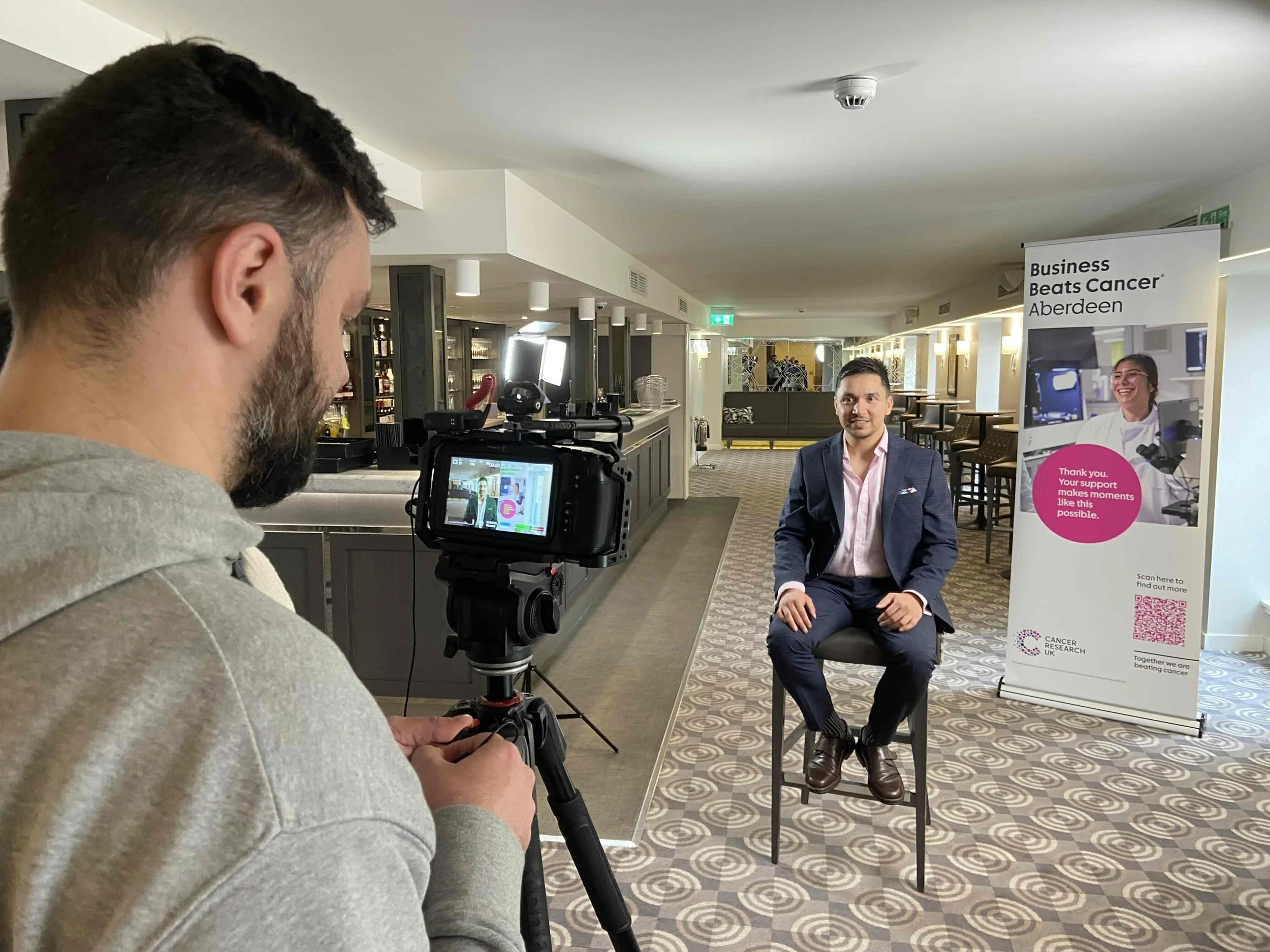 Farsight crew member filming a Business Beats Cancer Aberdeen board member beside the event banner.