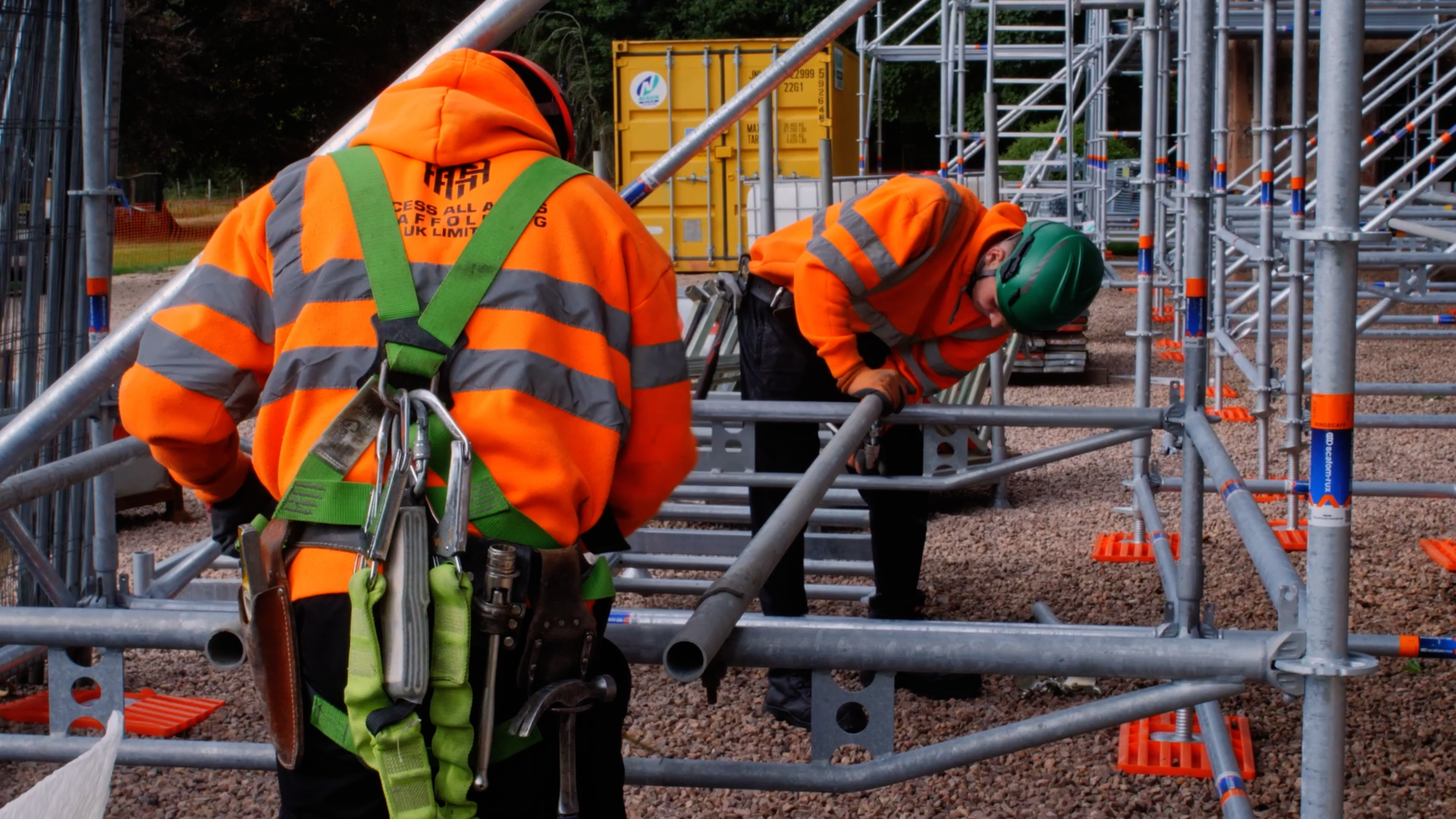 Two AAA Scaffolding workers assembling scaffold tubes on site.