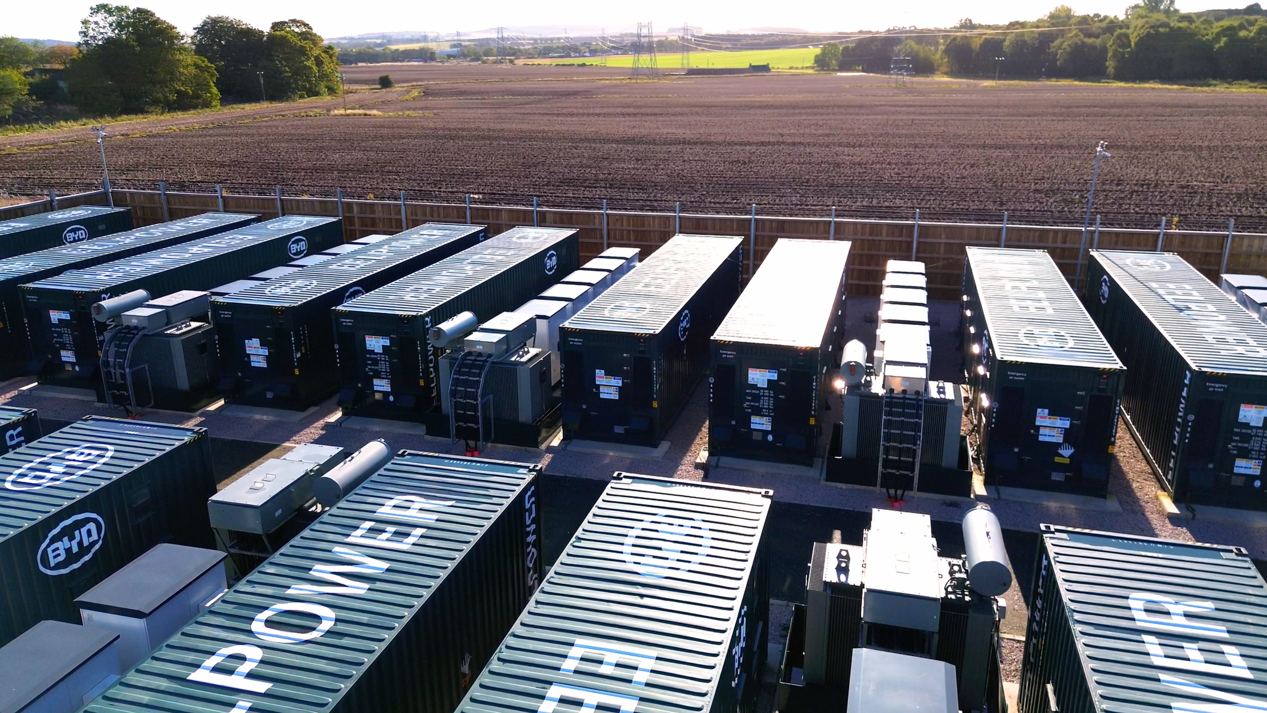 Green battery storage units positioned at an Ener-G Services site in a rural setting.