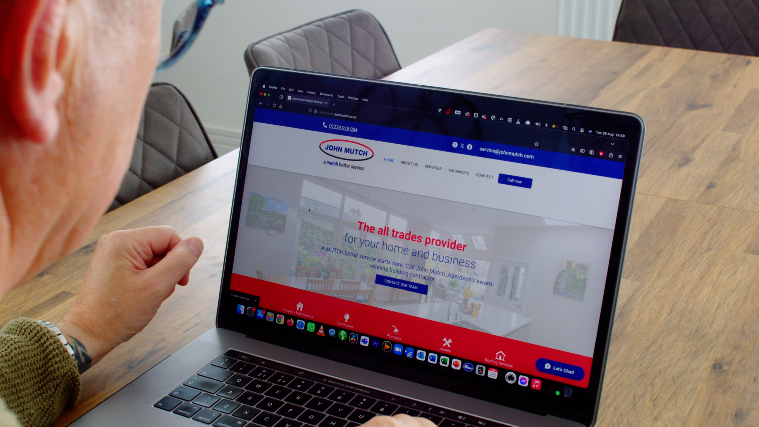 Man seated at a desk with the John Mutch Building Services website open on his laptop.
