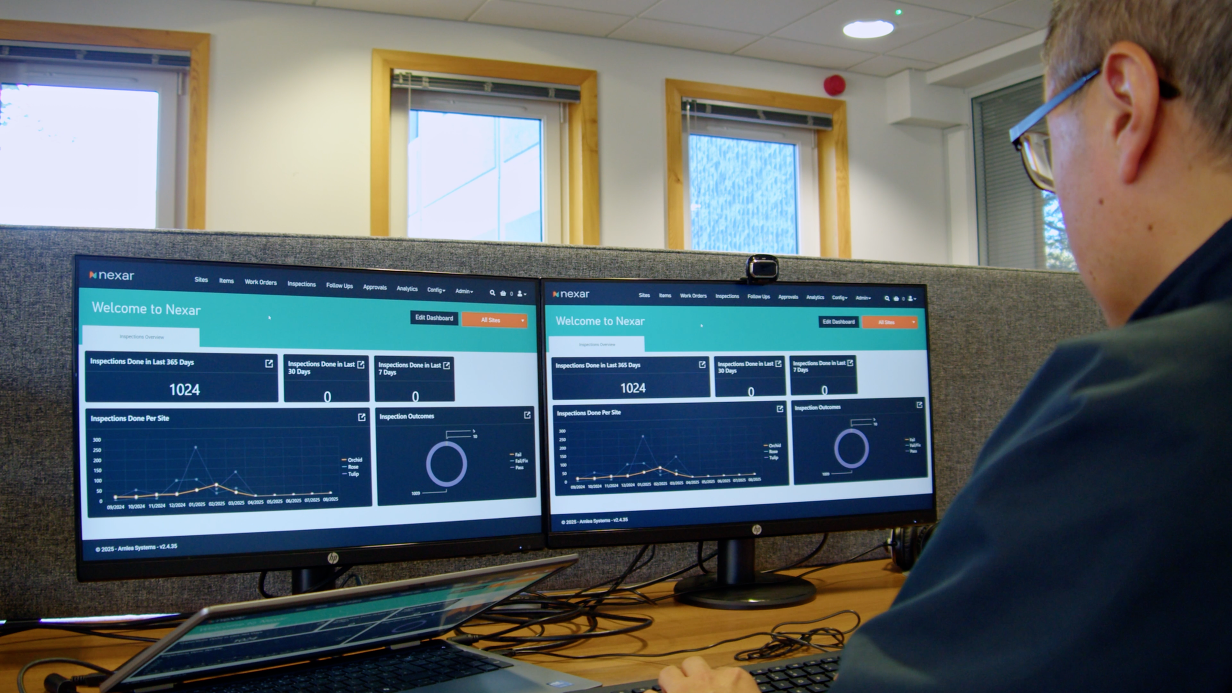 Arnlea Systems team member working across two monitors and a laptop with NEXAR dashboards and charts visible.