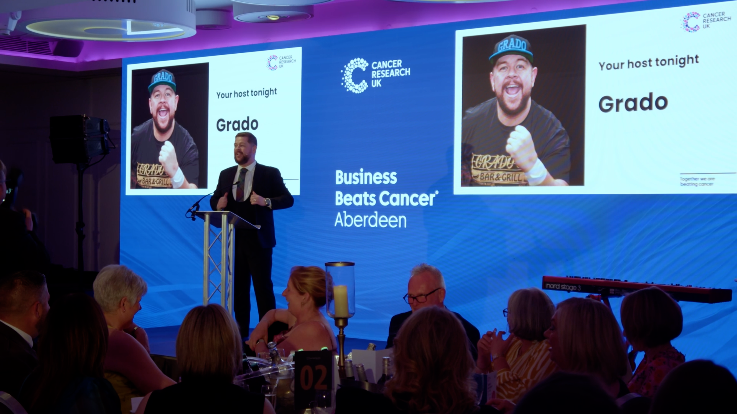 Grado speaking to the audience on stage at Business Beats Cancer Aberdeen.