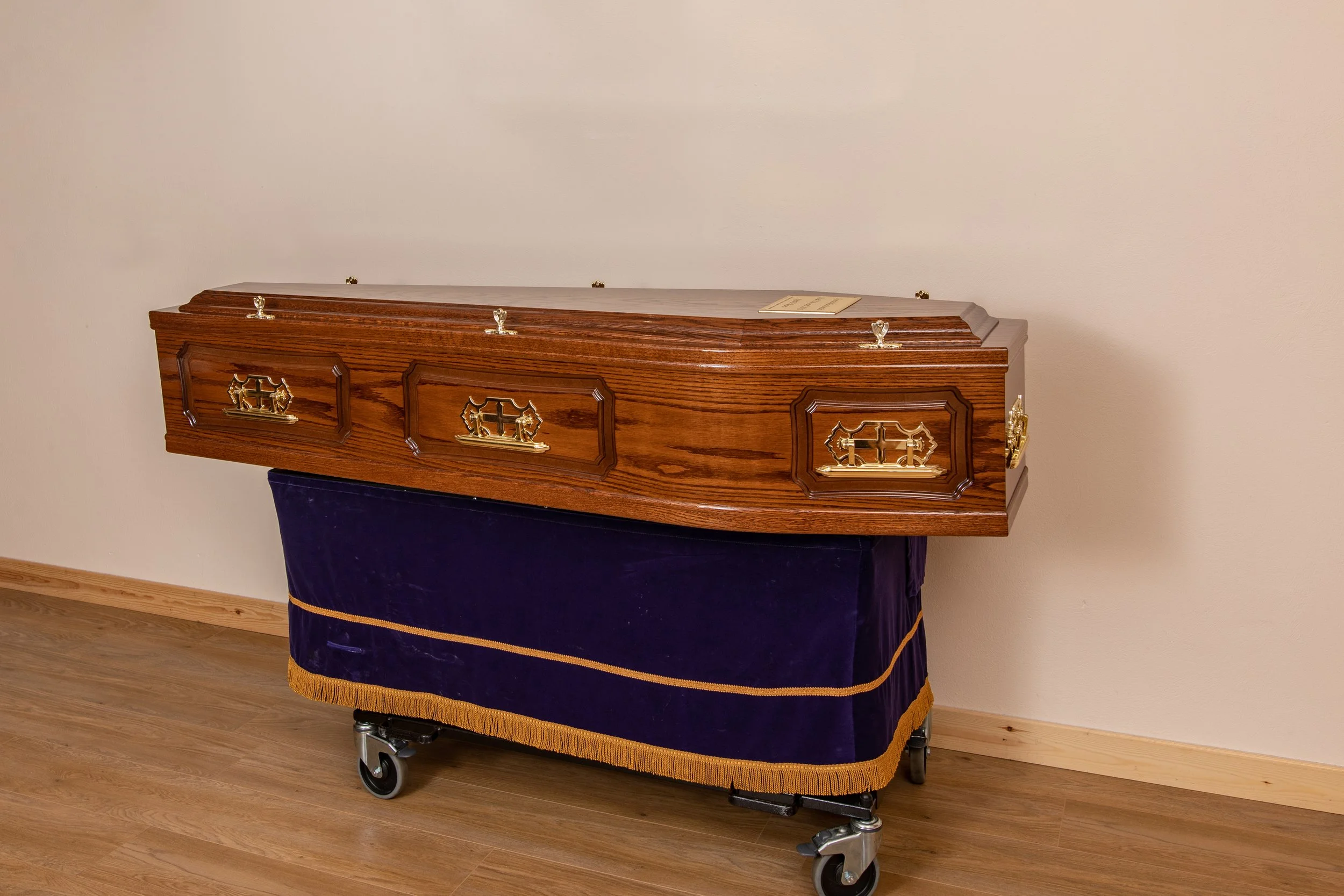 Raised lid panel side coffin dark oak veneer. Also available in light oak veneer. Full details: raised lid and panel sides, metal handles, engraved name plate, 8 cords. Comes complete with engraved garve marker as well as purple coffin cover to prote