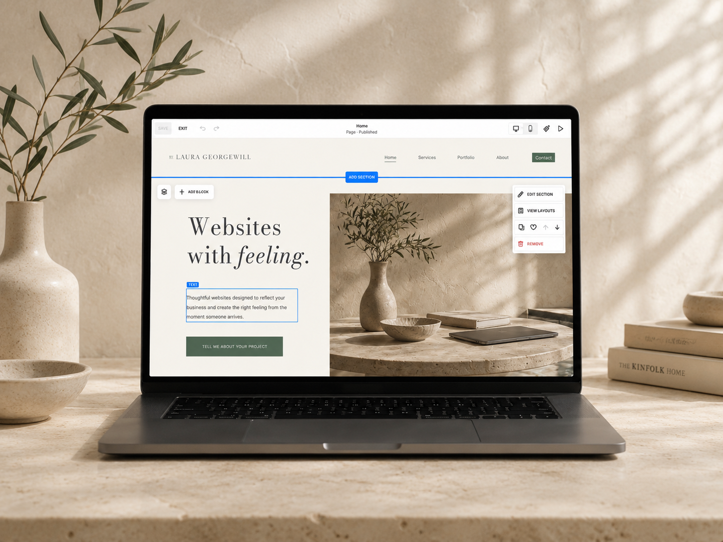 Laptop on a desk showing a website builder interface with a webpage titled 'Websites with feeling' and a background image of a beige textured wall decorated with a plant in a vase, some bowls, and books.
