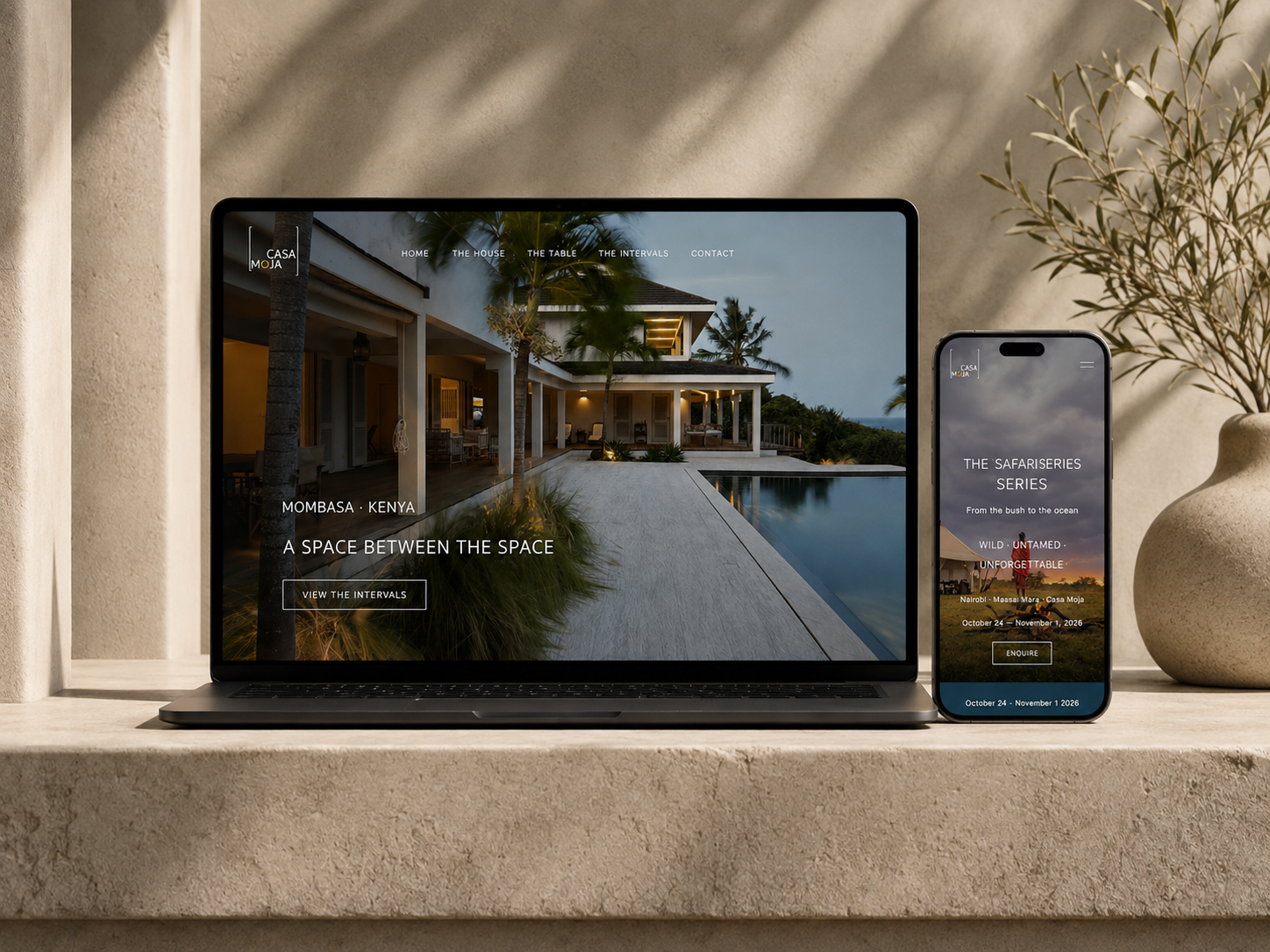 Laptop and smartphone displaying a luxurious house with a pool in Mombasa, Kenya, placed on a beige stone surface with a beige textured wall, potted plant, and shadowed background.