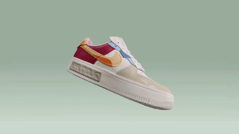 A colorful sneaker with a white sole, pink, red, yellow, blue, and cream panels, floating against a light green background.