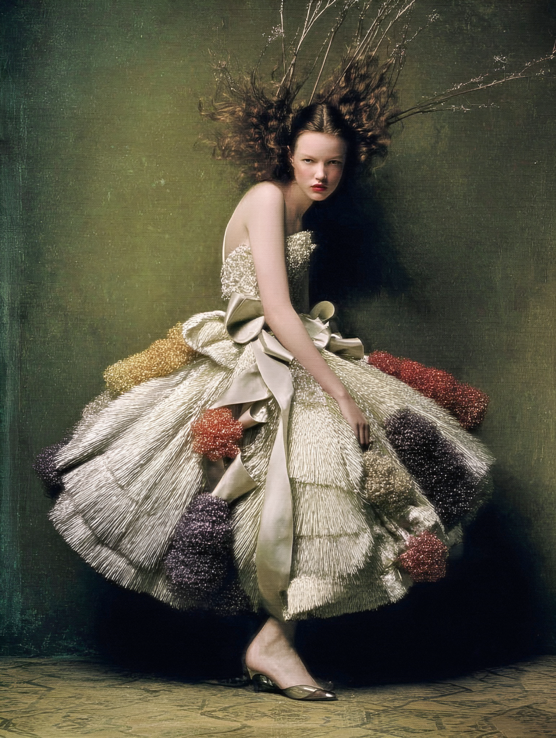A woman with curly hair floating above a dark background, wearing a large, ornate dress with a full skirt decorated with flowers and textured fabric, and her right leg behind her left leg in a dance pose.