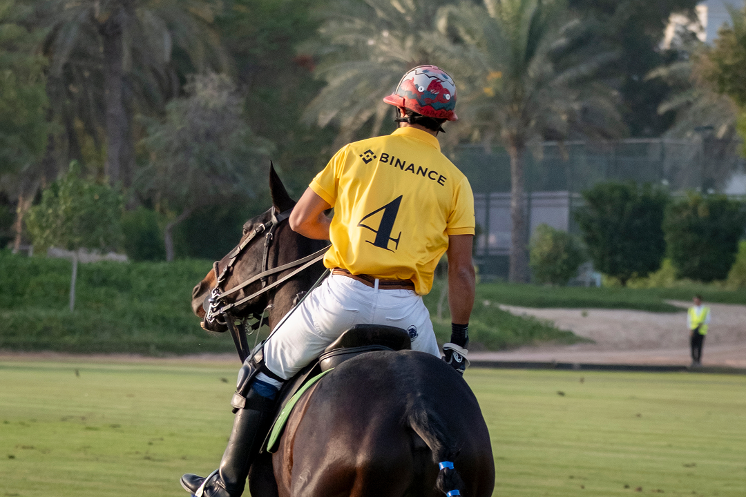 A polo player riding a dark horse on a grass field, wearing a yellow jersey with the number 4 and a helmet with a red and white pattern.