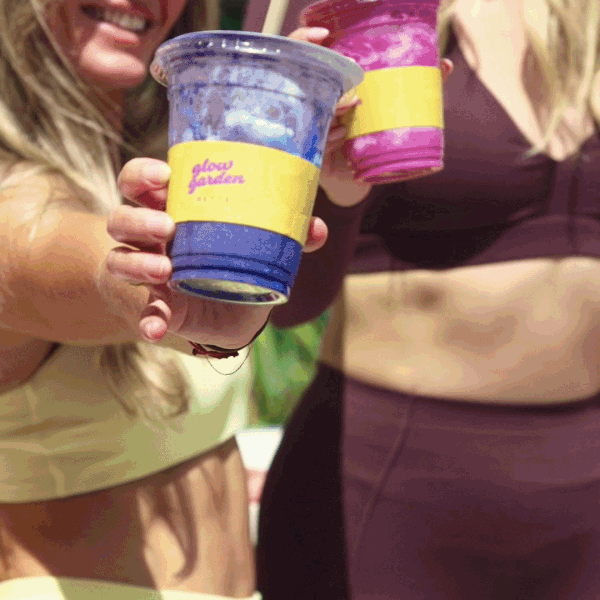 Two women holding colorful cups with painted designs, smiling and standing close together.
