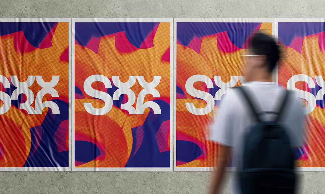 A person with a backpack looking at colorful abstract artwork posters on a gray concrete wall.