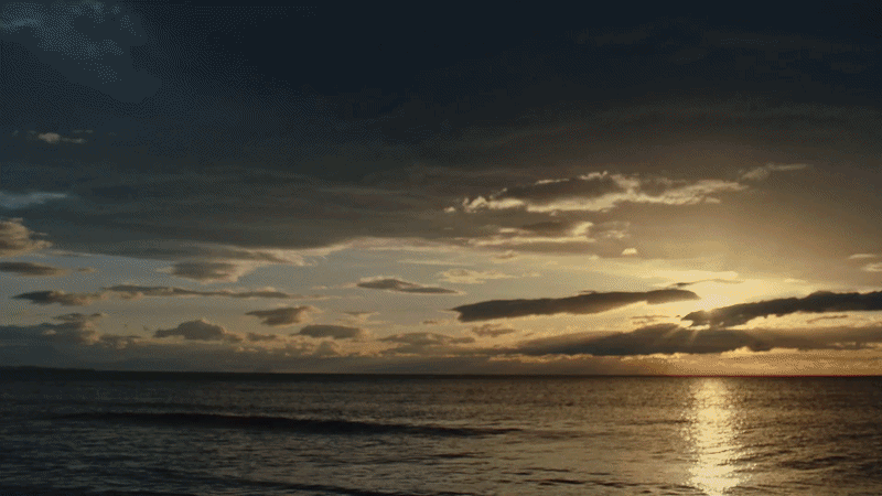 Sunset over the ocean with dark clouds and a calm sea.
