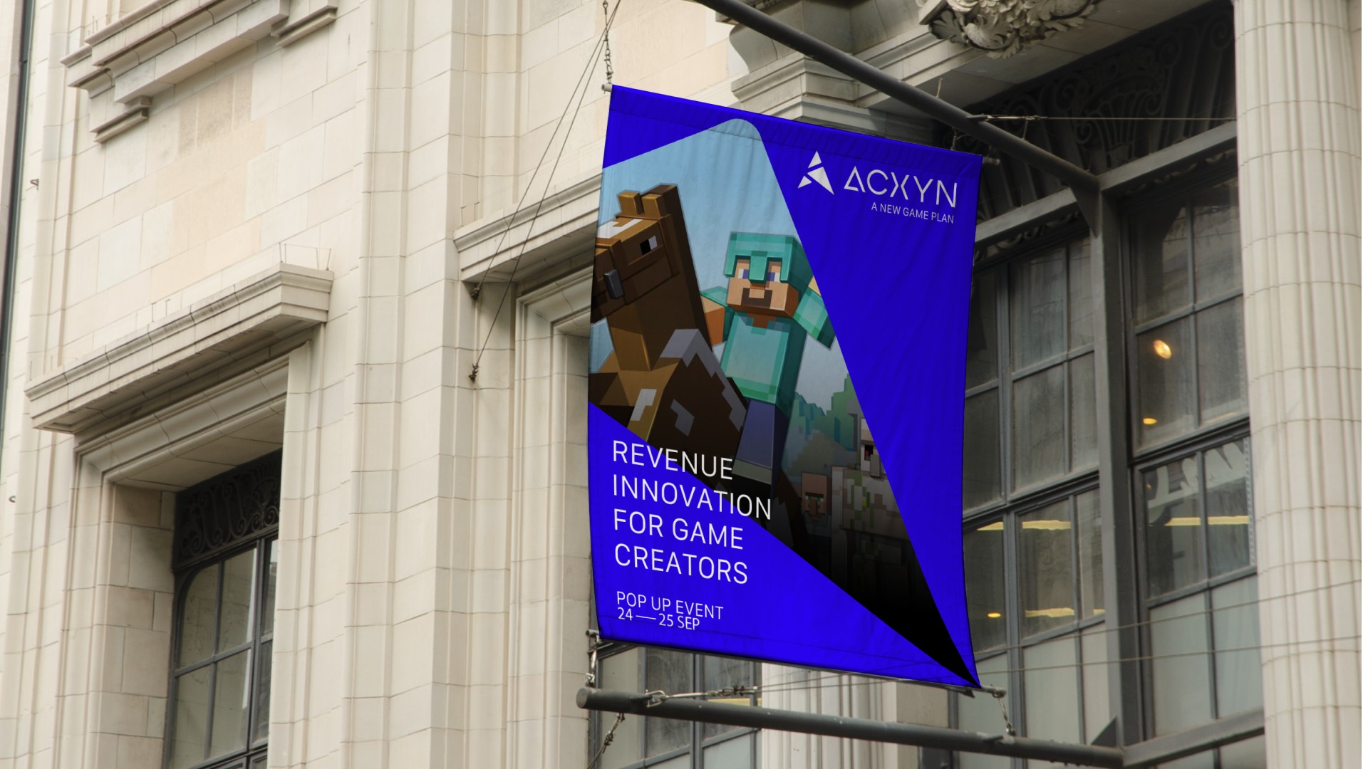 A vertical banner hanging outside a building, advertising a gaming event by Acxyn. The banner features pixel art of a character from Minecraft with a pickaxe and a horse, with text promoting revenue and innovation for game creators. The event is a po
