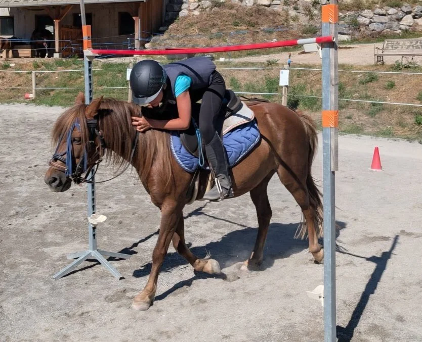 Un enfant à cheval, portant un casque, franchissant un obstacle d'équitation dans un centre équestre.