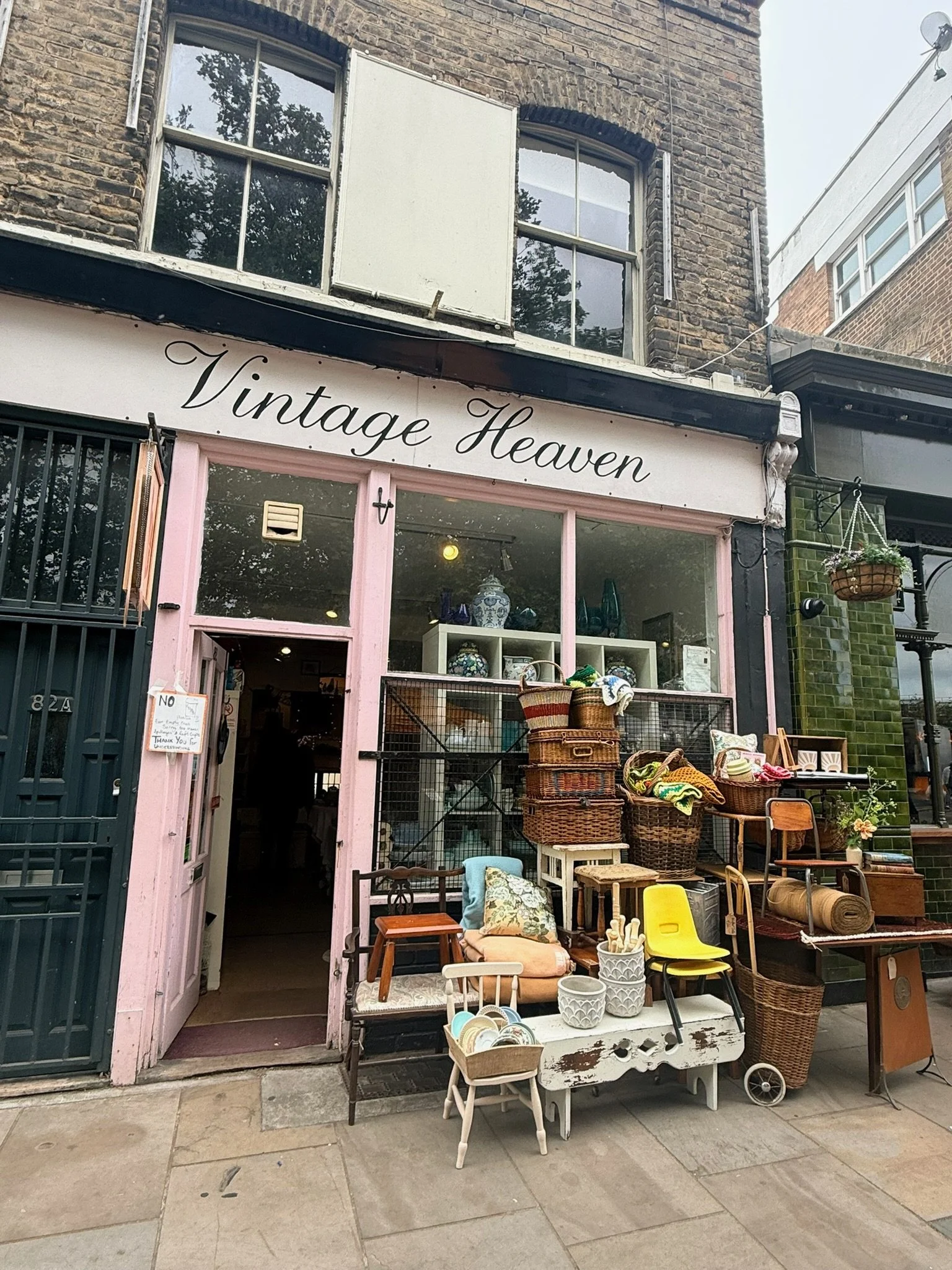 Outside vintage thrift store called 'Vintage Heaven' with displays of furniture, baskets, and decorative items on the sidewalk.