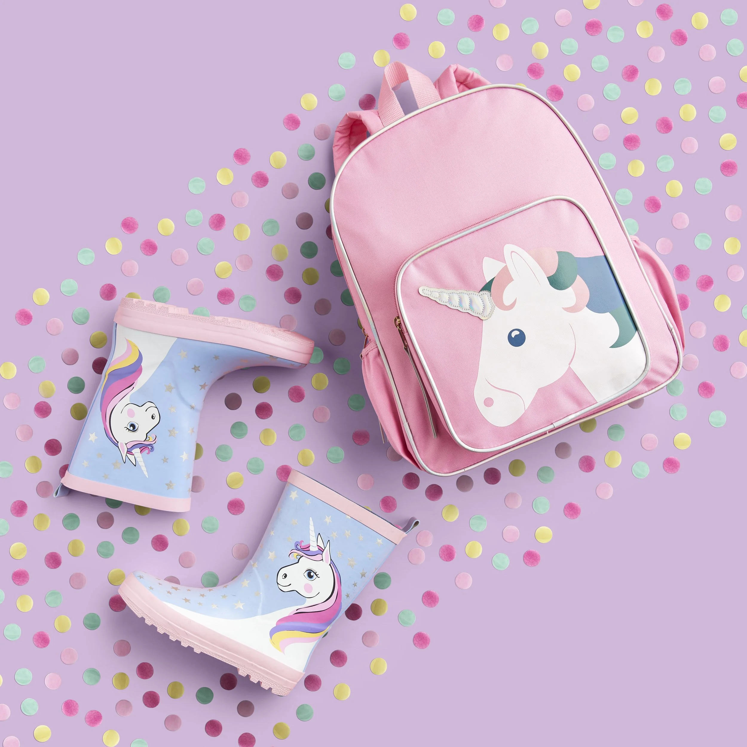 Pink backpack with unicorn design on a purple background, surrounded by pastel-colored confetti and a unicorn-shaped party hat.