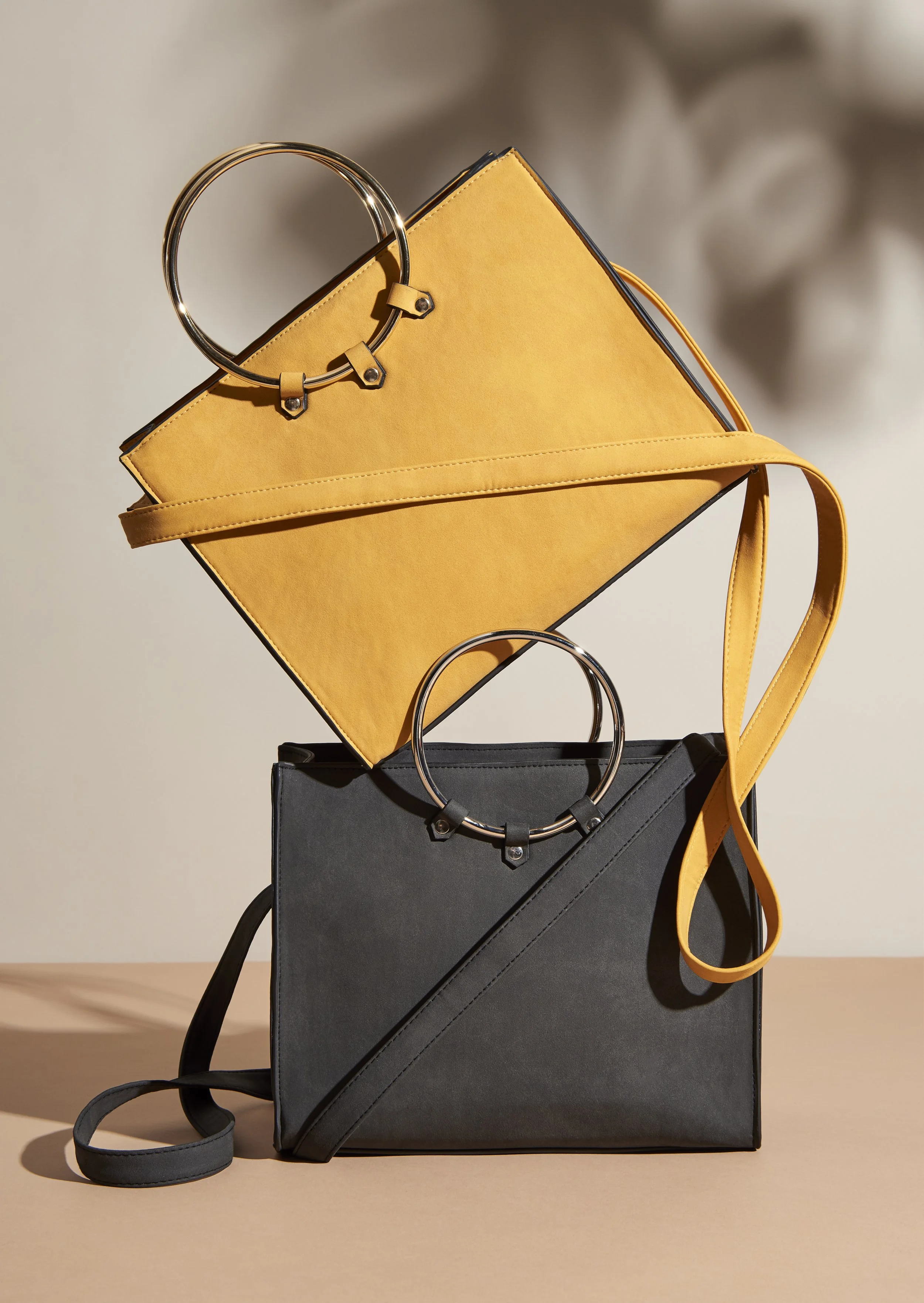 Stacked black and yellow handbags with circular metal handles on a beige surface.