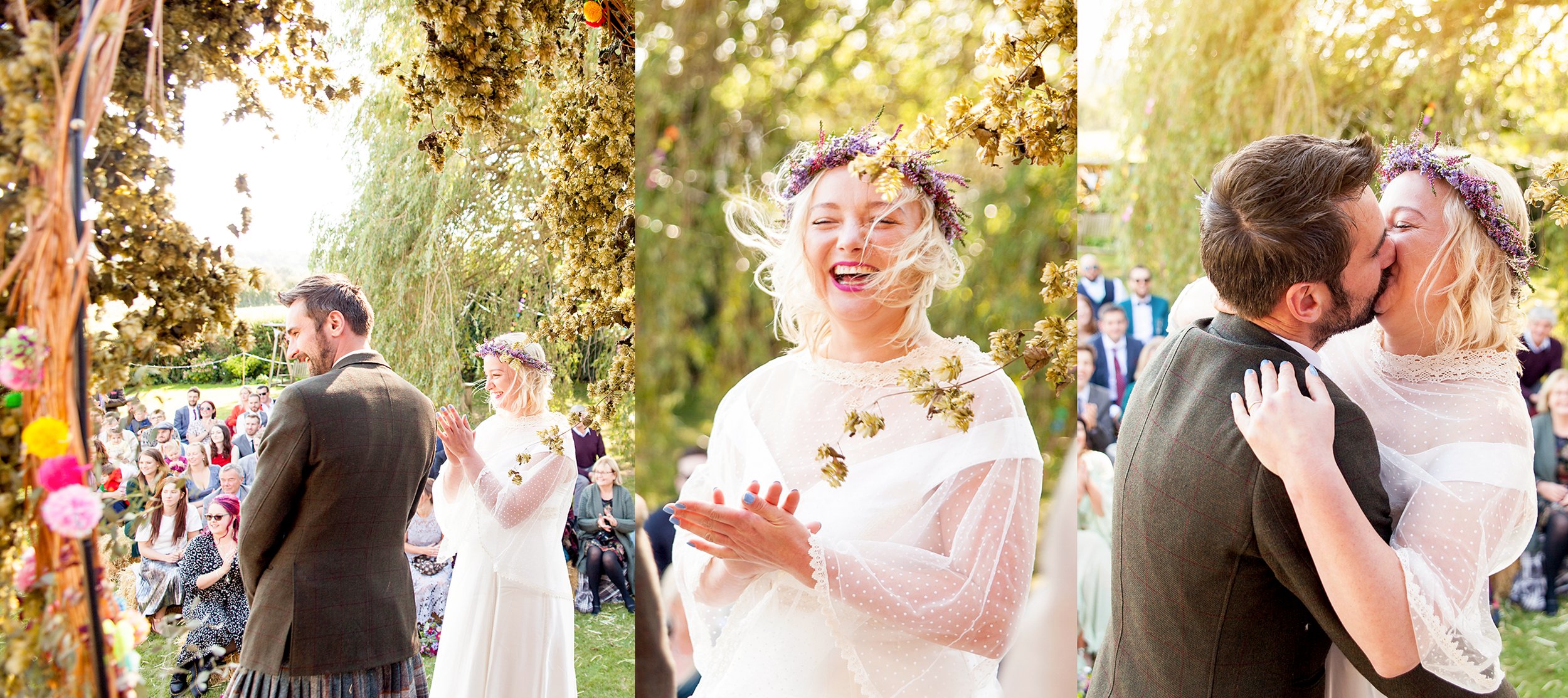 A wedding ceremony outdoors with a groom and bride exchanging vows, surrounded by seated guests. The bride is wearing a white lace dress and a floral crown, while the groom is in a plaid suit. The bride smiles joyfully, and they share a kiss later in the event.