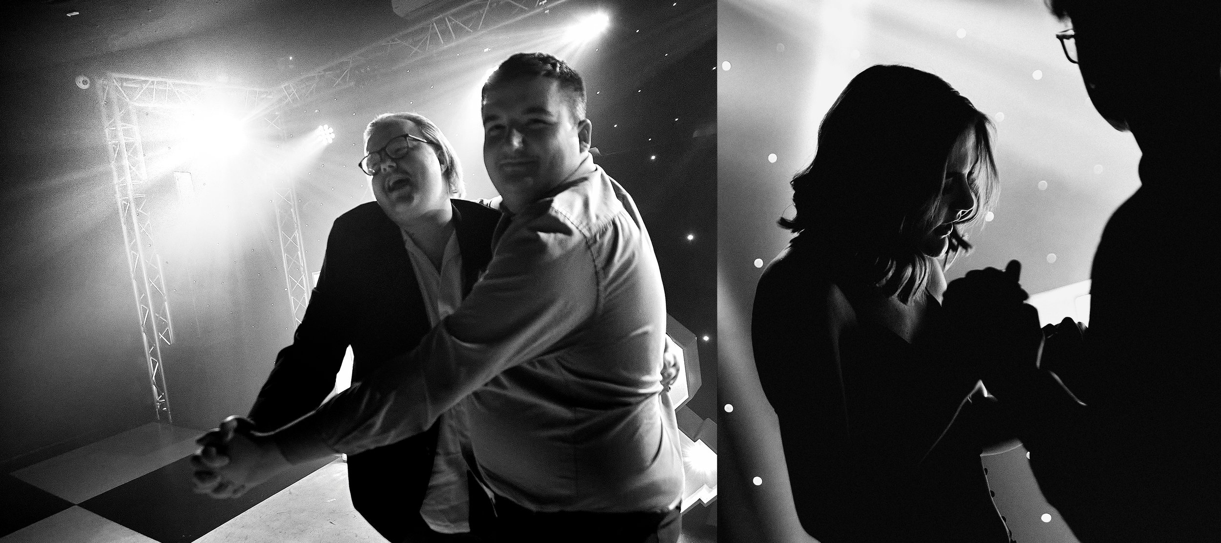 Black and white photo of two couples dancing closely at a party or nightclub, with one woman wearing glasses. Bright stage lights and a metal truss structure are visible in the background.