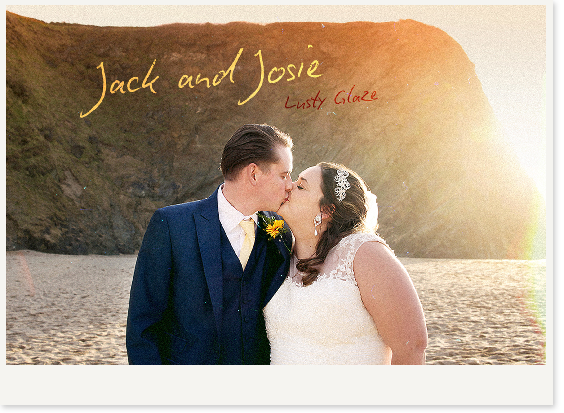 A bride and groom kissing on a beach at sunset with a rocky cliff in the background.