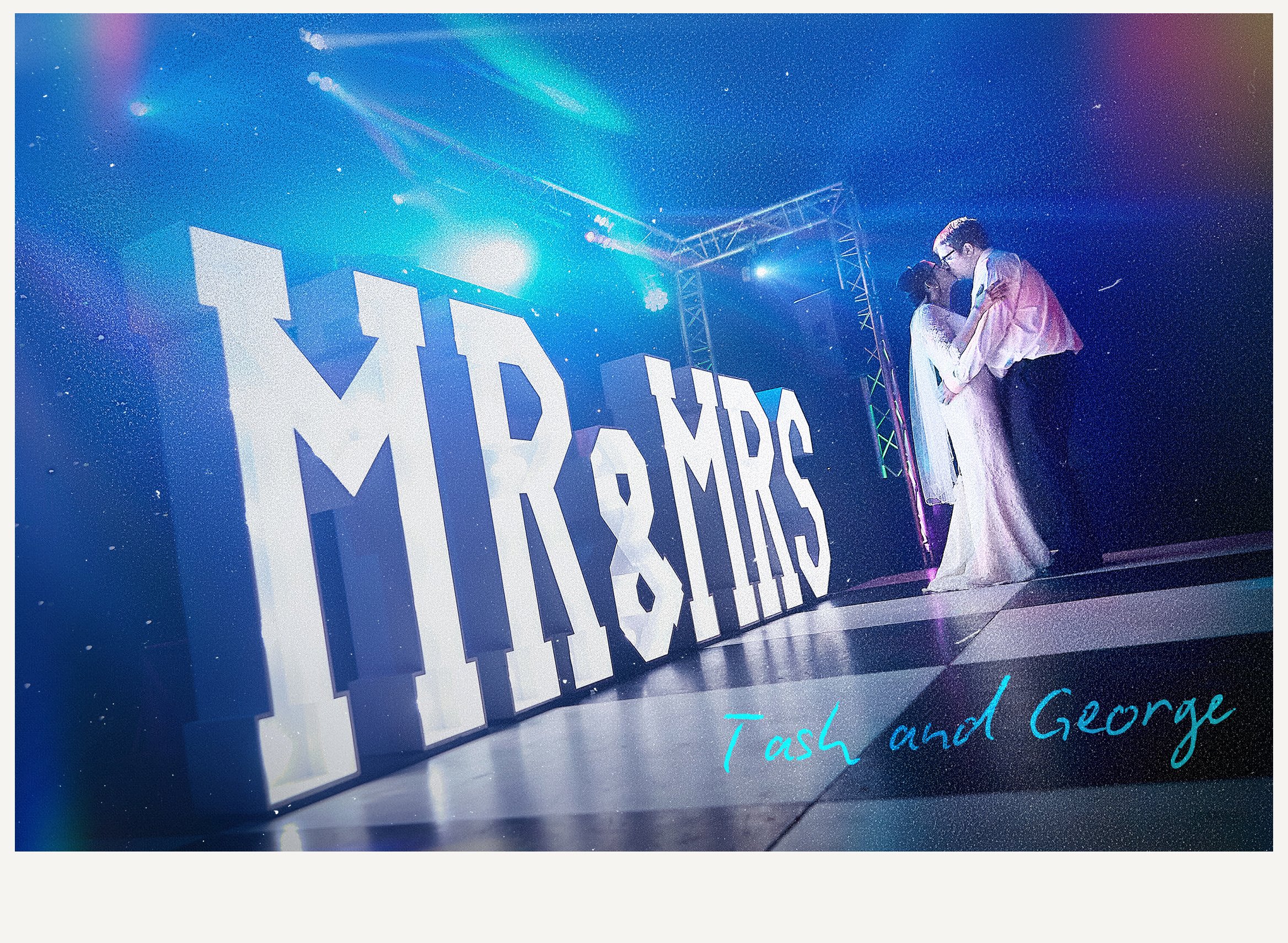 A promotional sign with large white letters spelling "MADAME" and blue cursive text reading "Task and George" underneath, illuminated by bright stage lights at an event or performance.