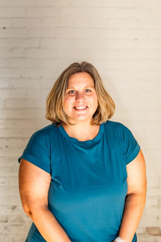 Headshot of Jenny Ellison in a Blue shirt on a white brick background