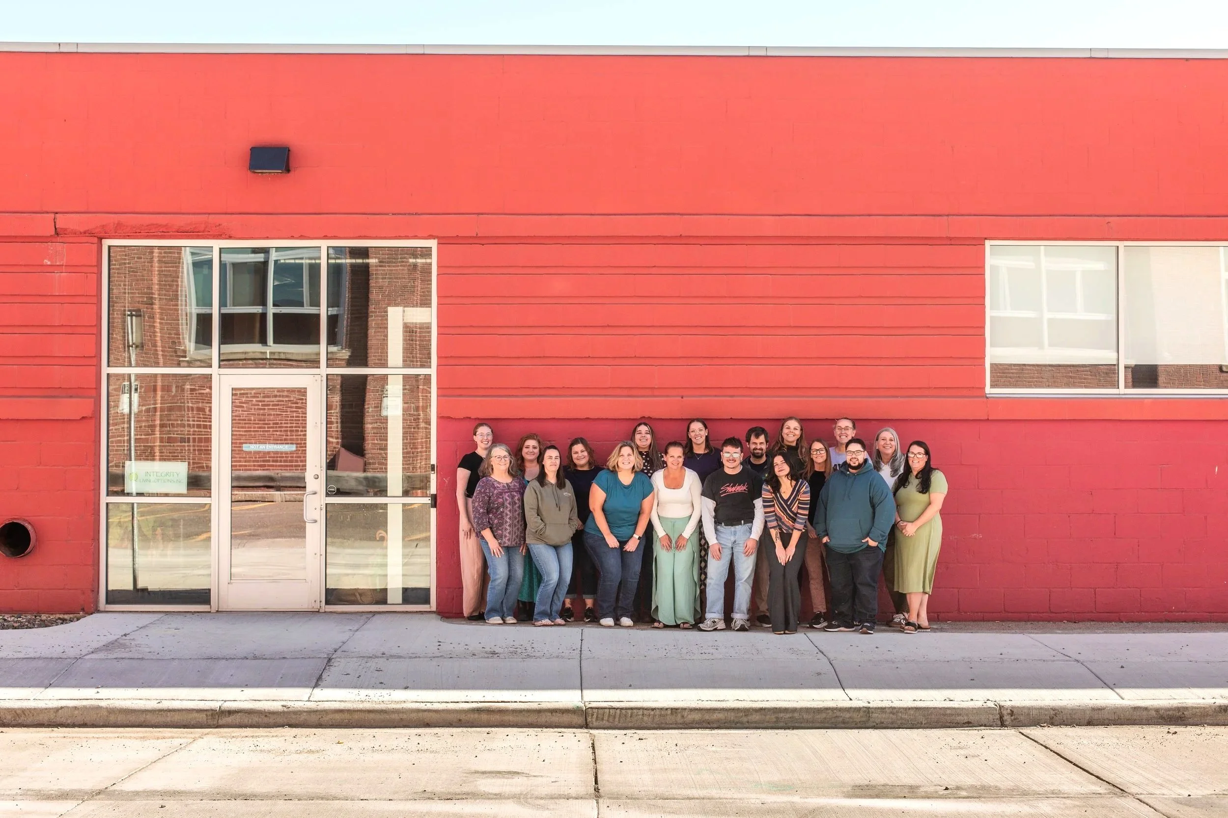 The ILO team standing together in front of the red office building with large glass doors and windows.